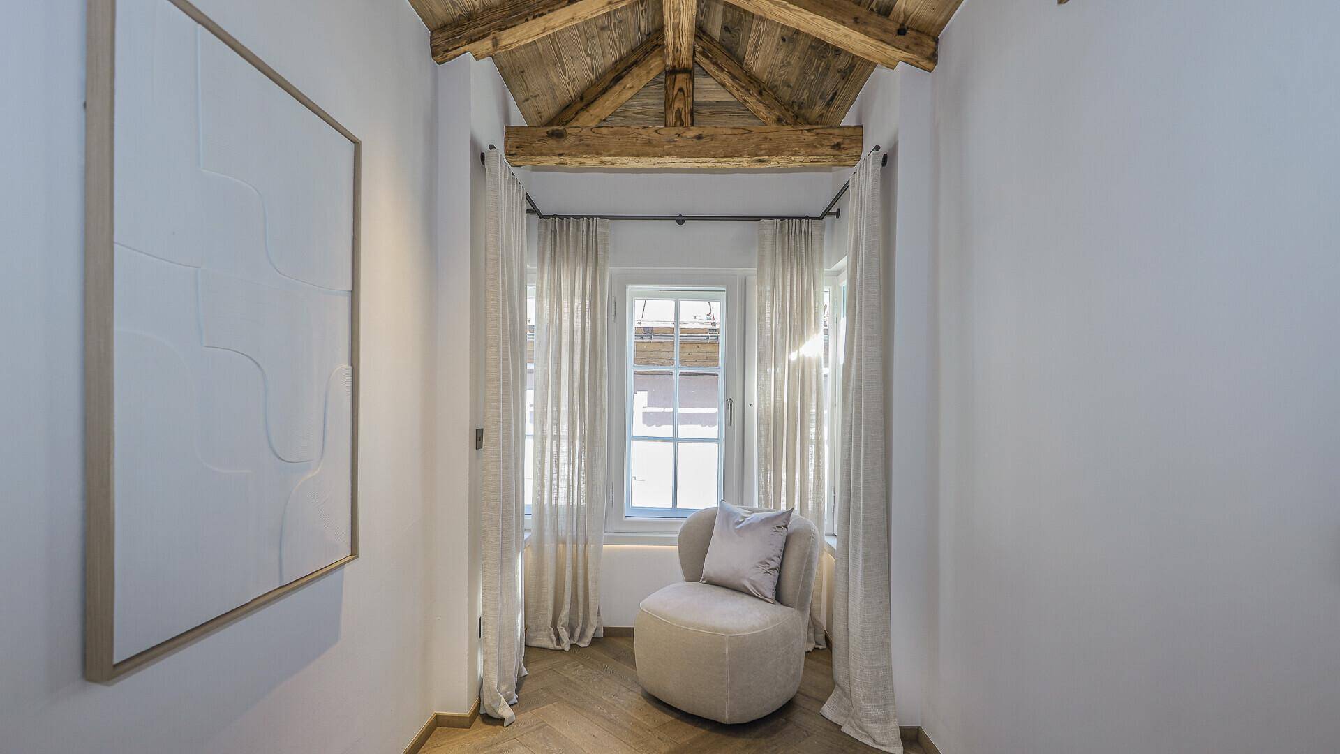 Heller Flurbereich mit einem Sessel, Fenster und Holzbalkendecke.
