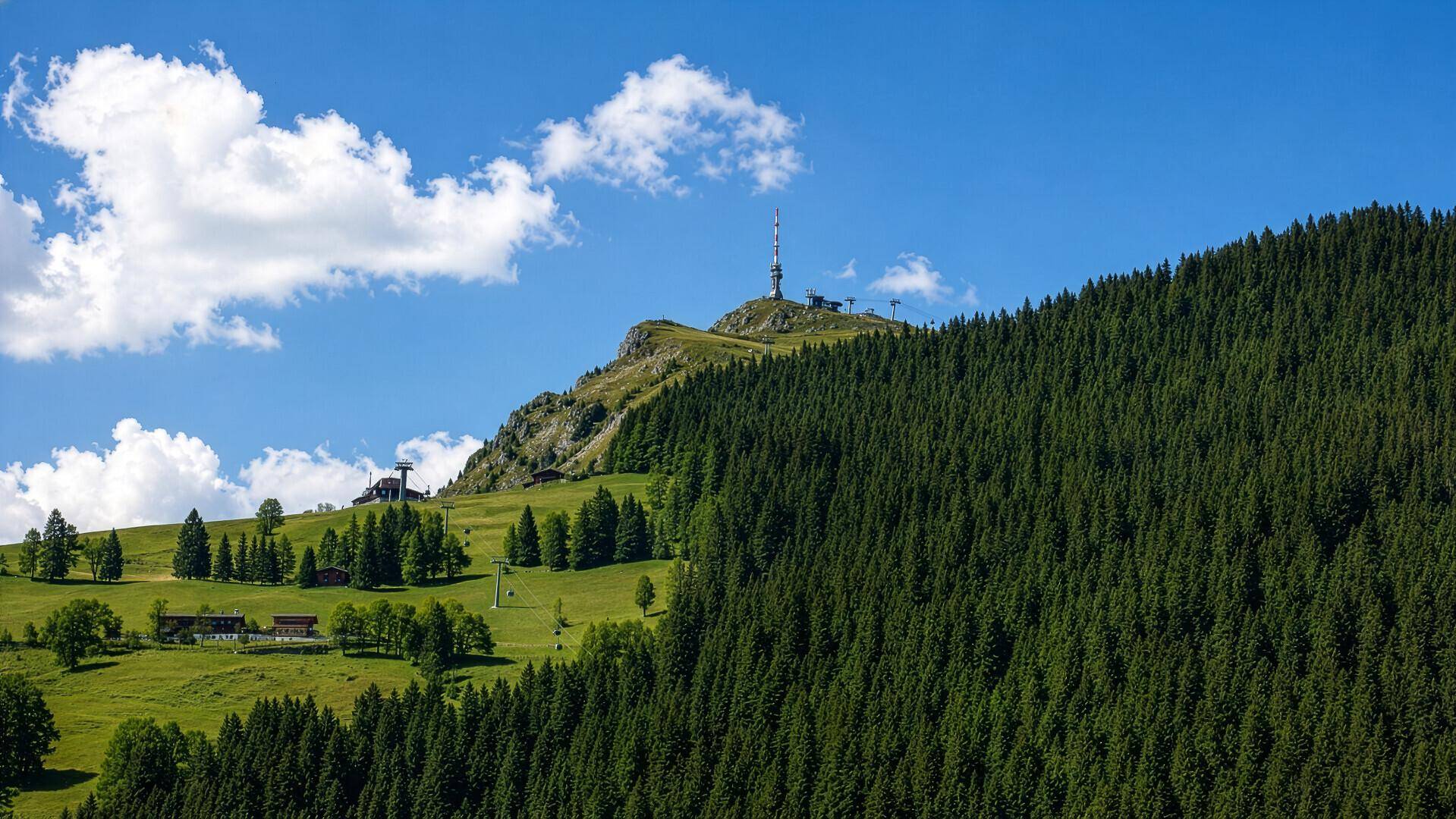 Malerische Berglandschaft mit grünen Wäldern und einem Sendeturm auf dem Gipfel.