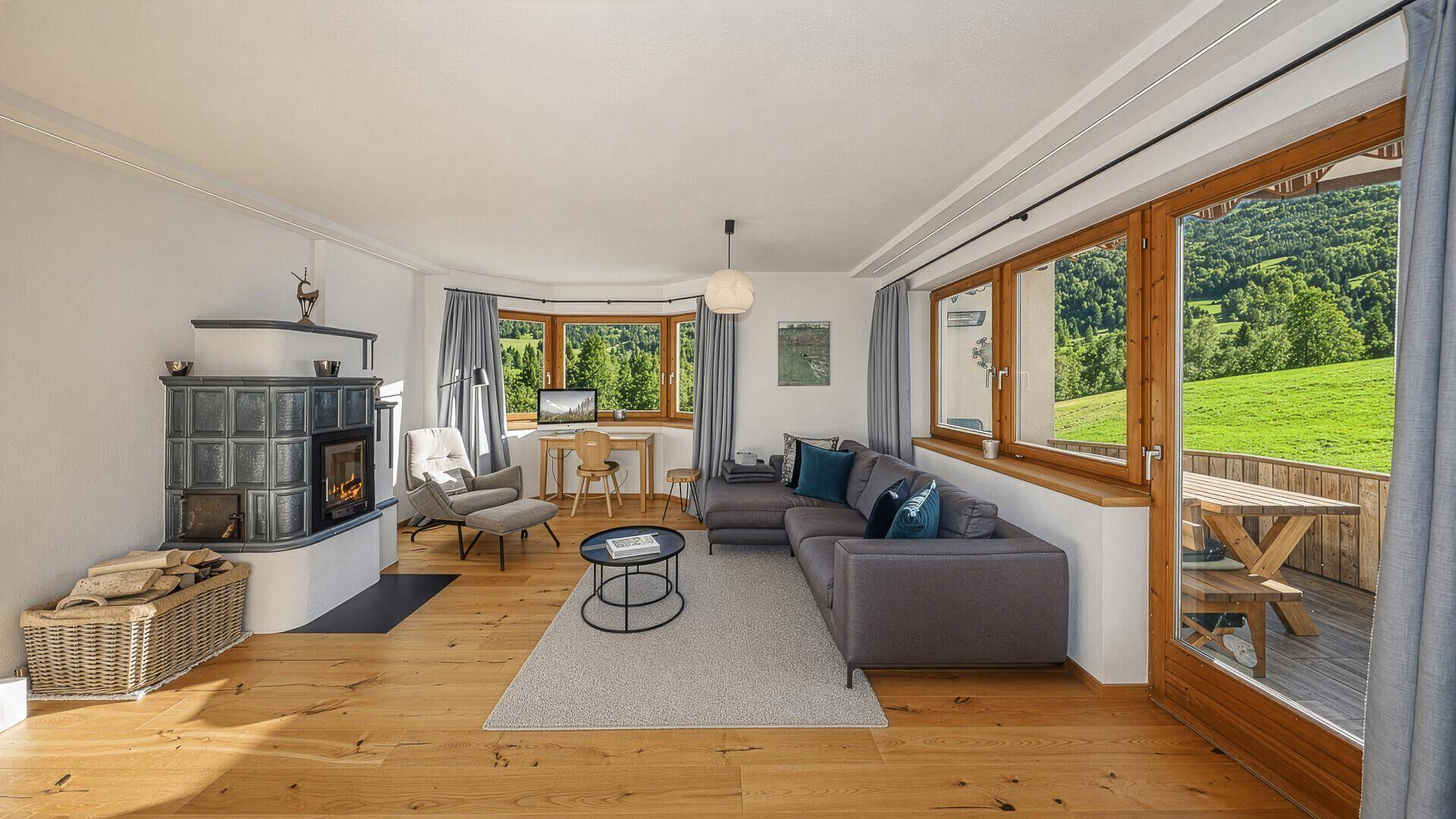 Geräumiges Wohnzimmer mit Kachelofen, Holzboden und Zugang zu einer Terrasse mit Bergblick.