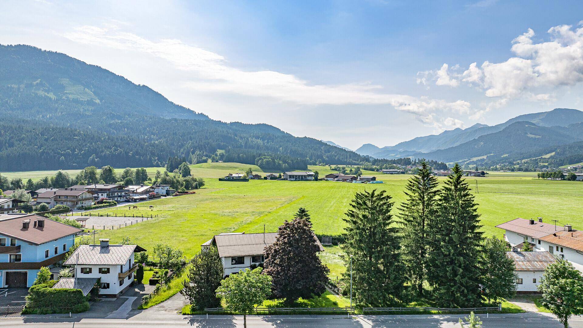Weitläufige Ansicht der ländlichen Umgebung mit Häusern, Feldern und der imposanten Bergkette.