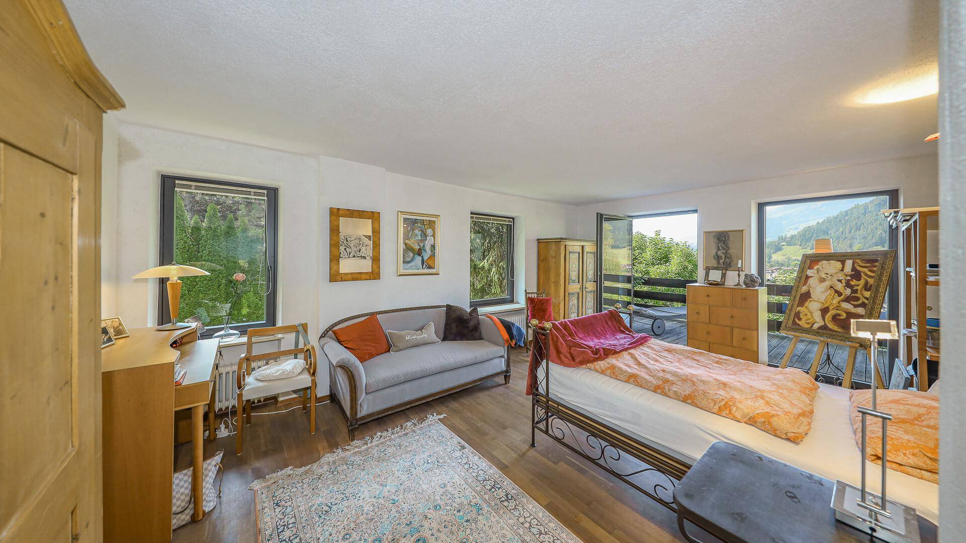 Helles Schlafzimmer mit Holzboden, Schreibtisch und Zugang zu einem Balkon mit Aussicht.