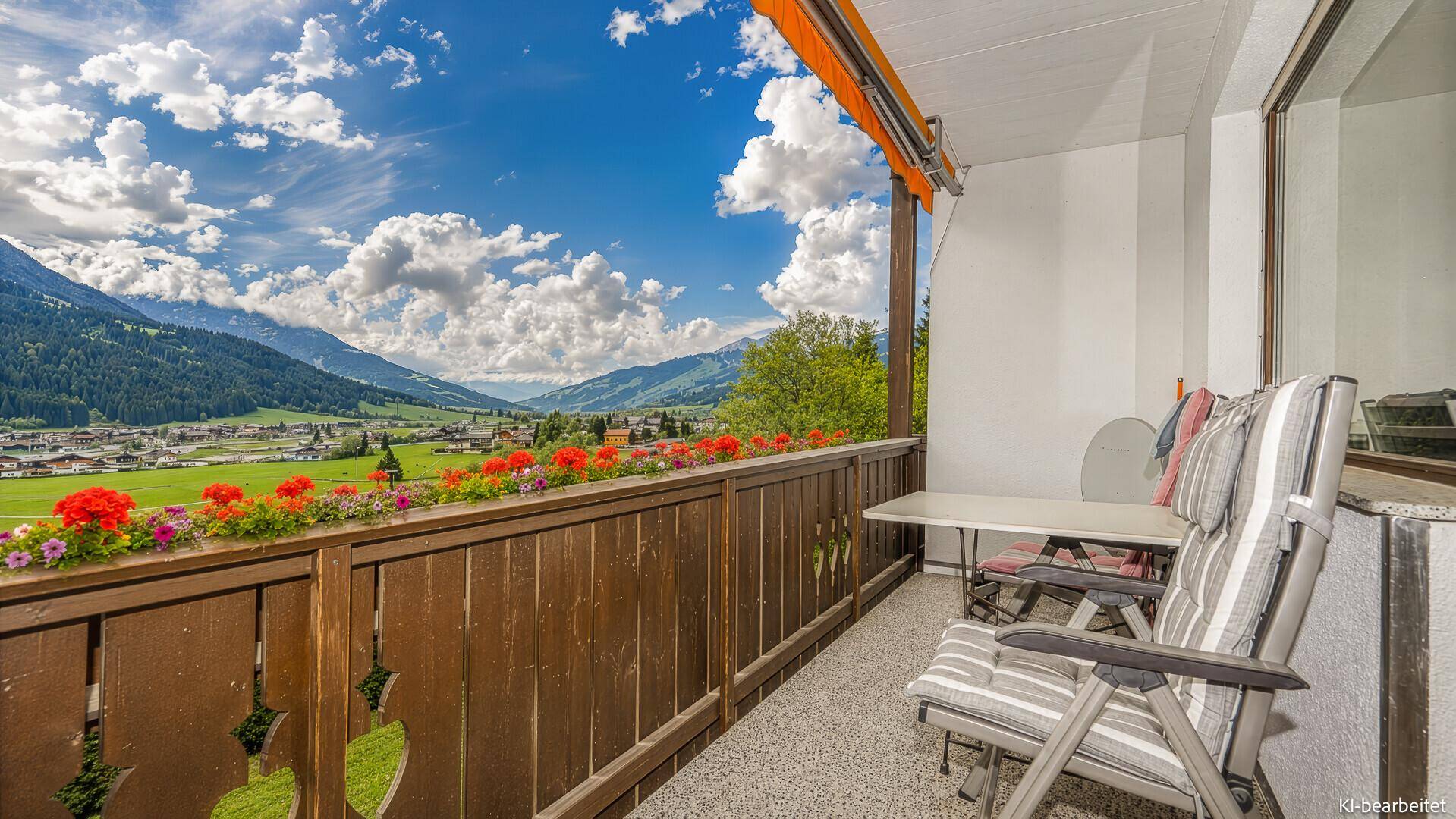 Sonniger Balkon mit Tisch und Stühlen, umgeben von Blumen und mit Bergblick.