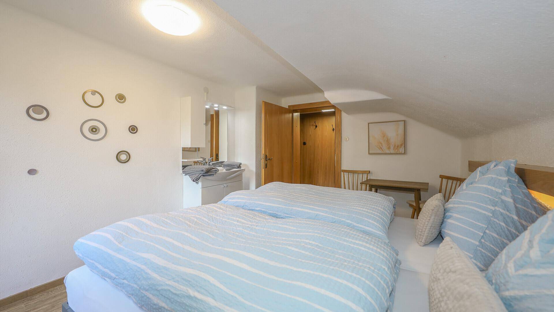 Dachgeschoss-Schlafzimmer mit schräger Decke, Doppelbett und integriertem Waschbecken.