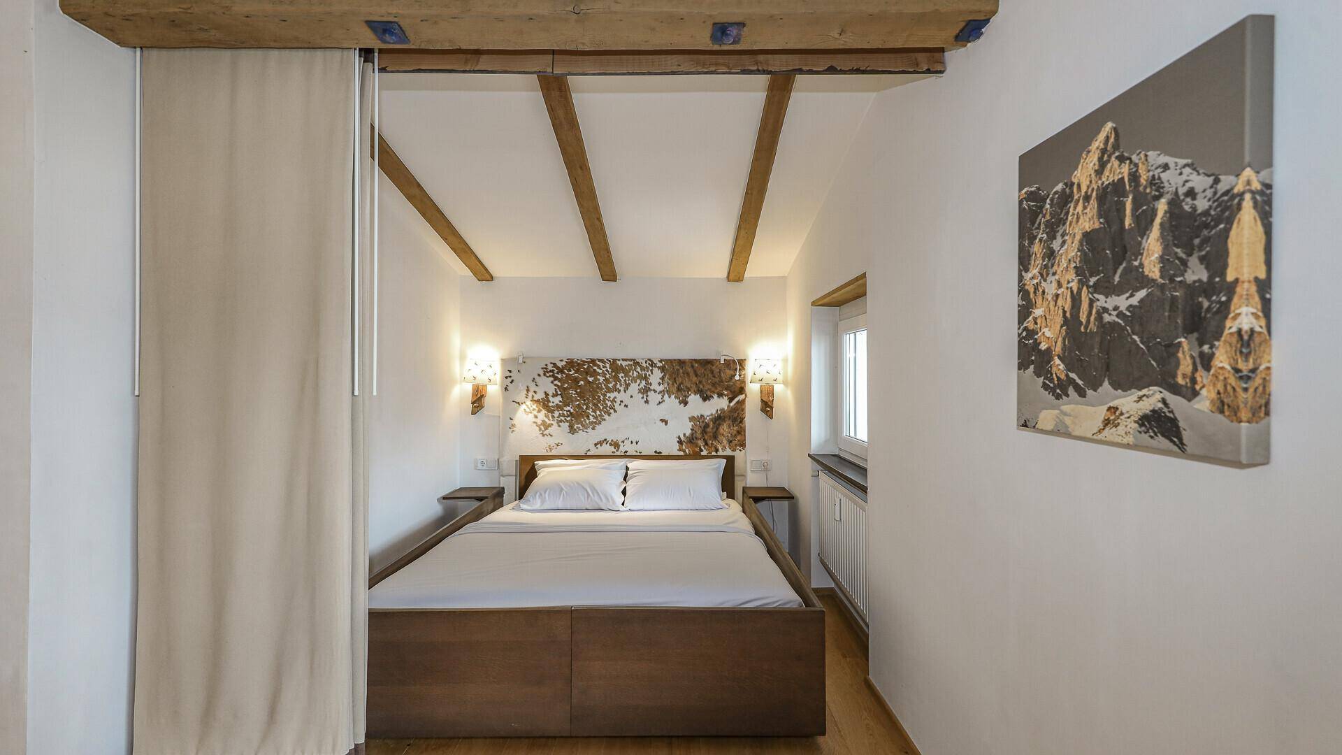 Gemütliches Schlafzimmer mit Holzbett, Holzbalkendecke und alpiner Dekoration.