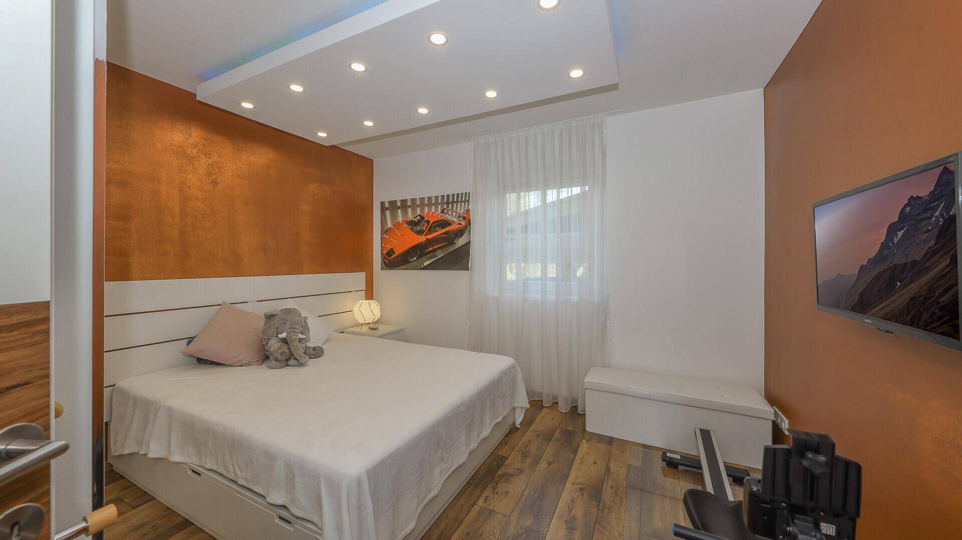 Helles Schlafzimmer mit farbiger Akzentwand, modernem Bett und Blick ins Freie.