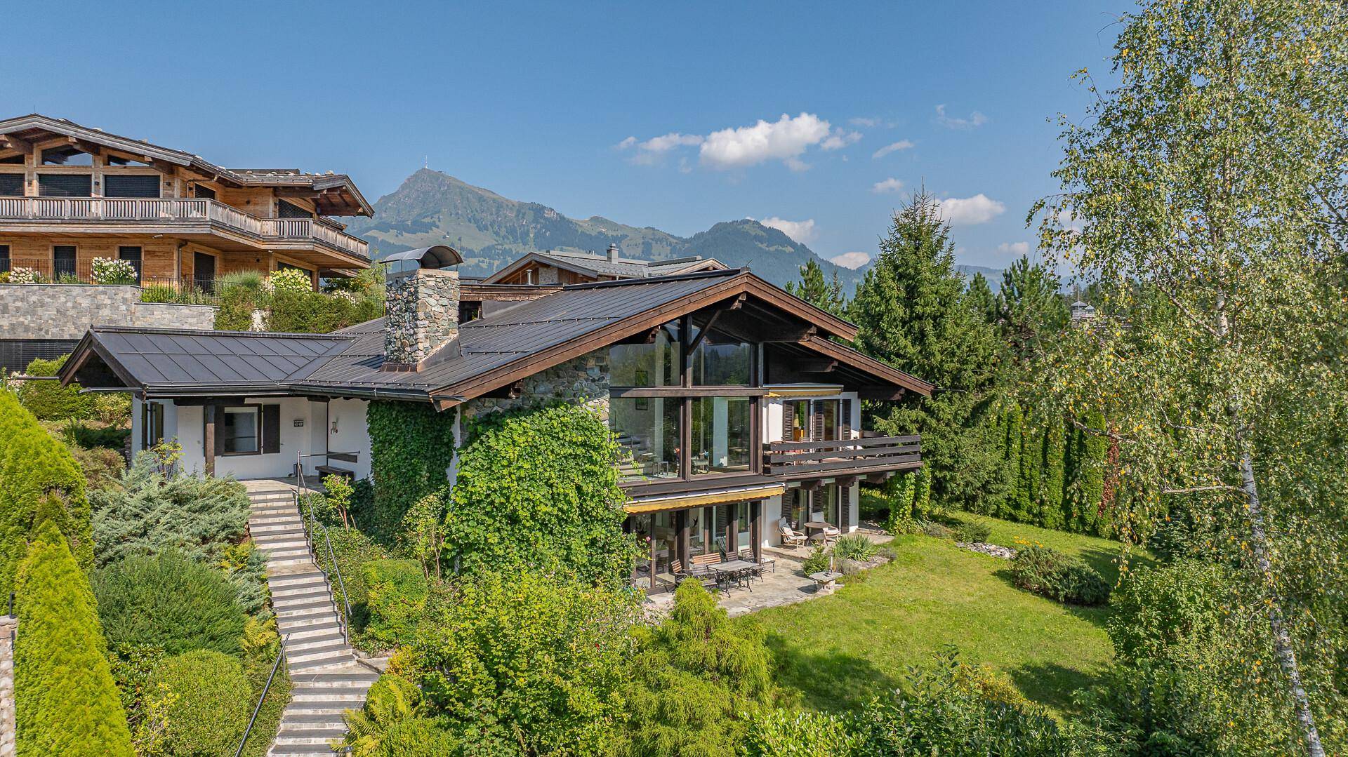 Charmantes Chalet mit Stein- und Holzfassade, umgeben von viel Grün und Bergblick.