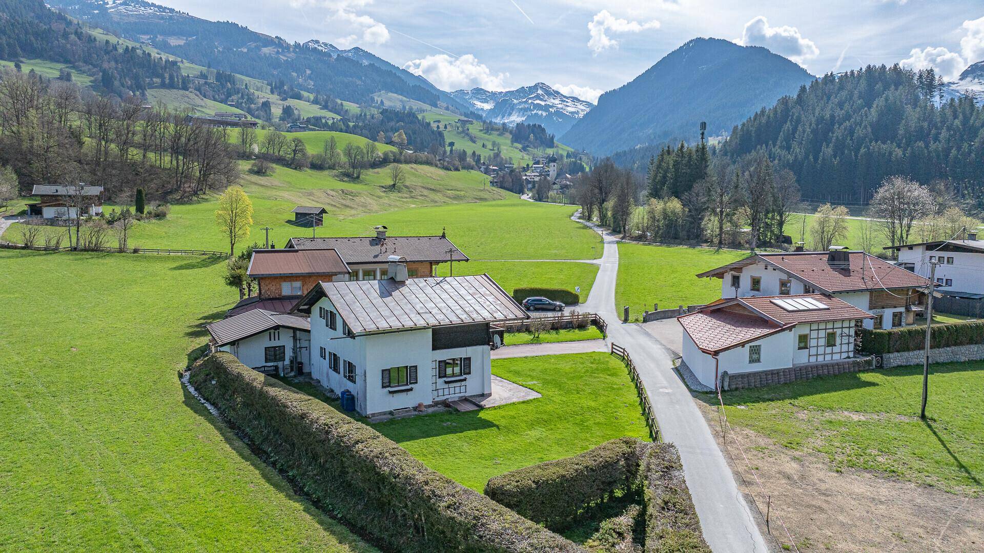 Luftaufnahme des Hauses in einer malerischen Berglandschaft mit grünen Wiesen und umliegenden Häusern.