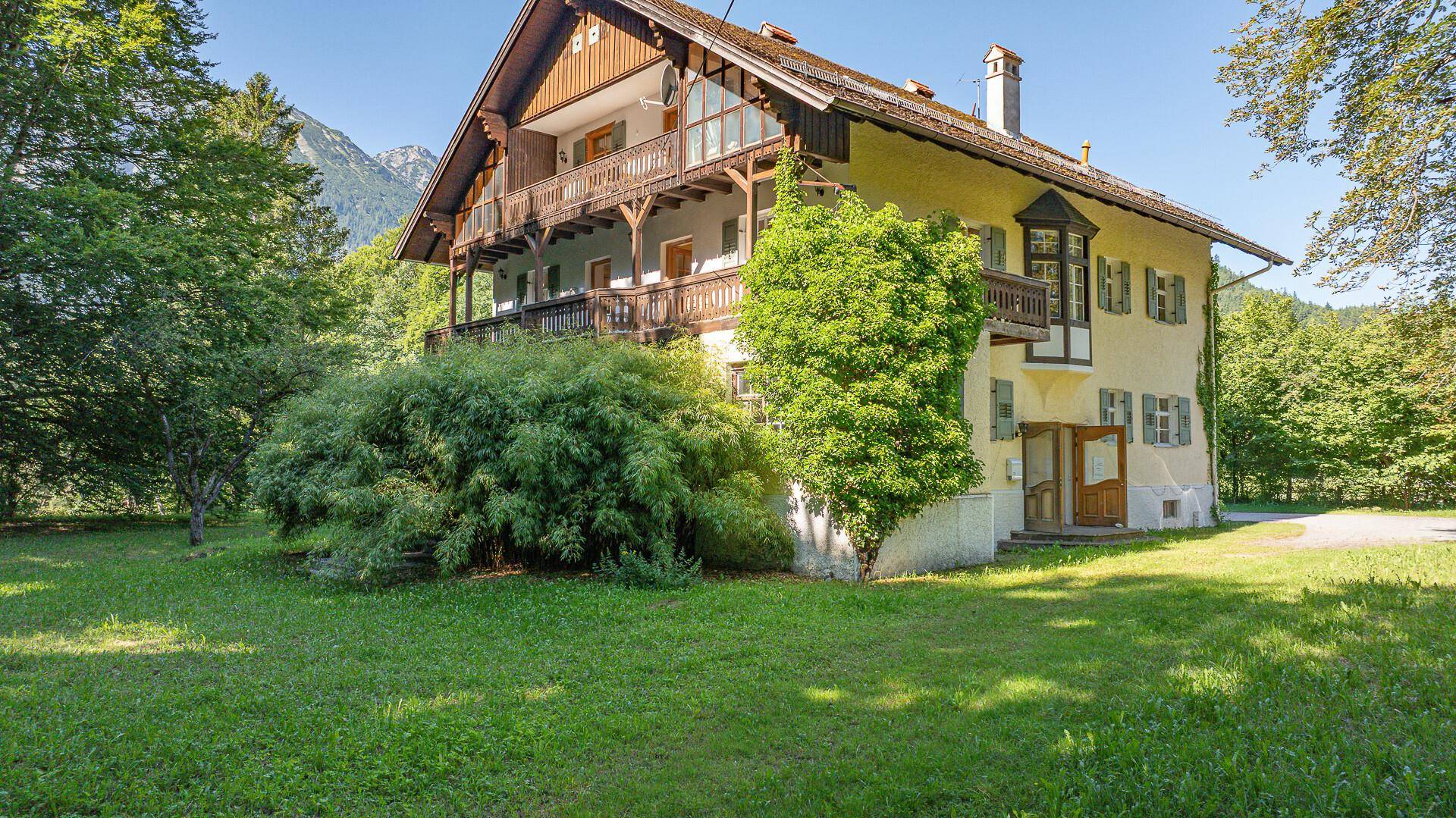 Traditionelles Haus mit mehreren Balkonen, umgeben von viel Grün und mit Bergblick.