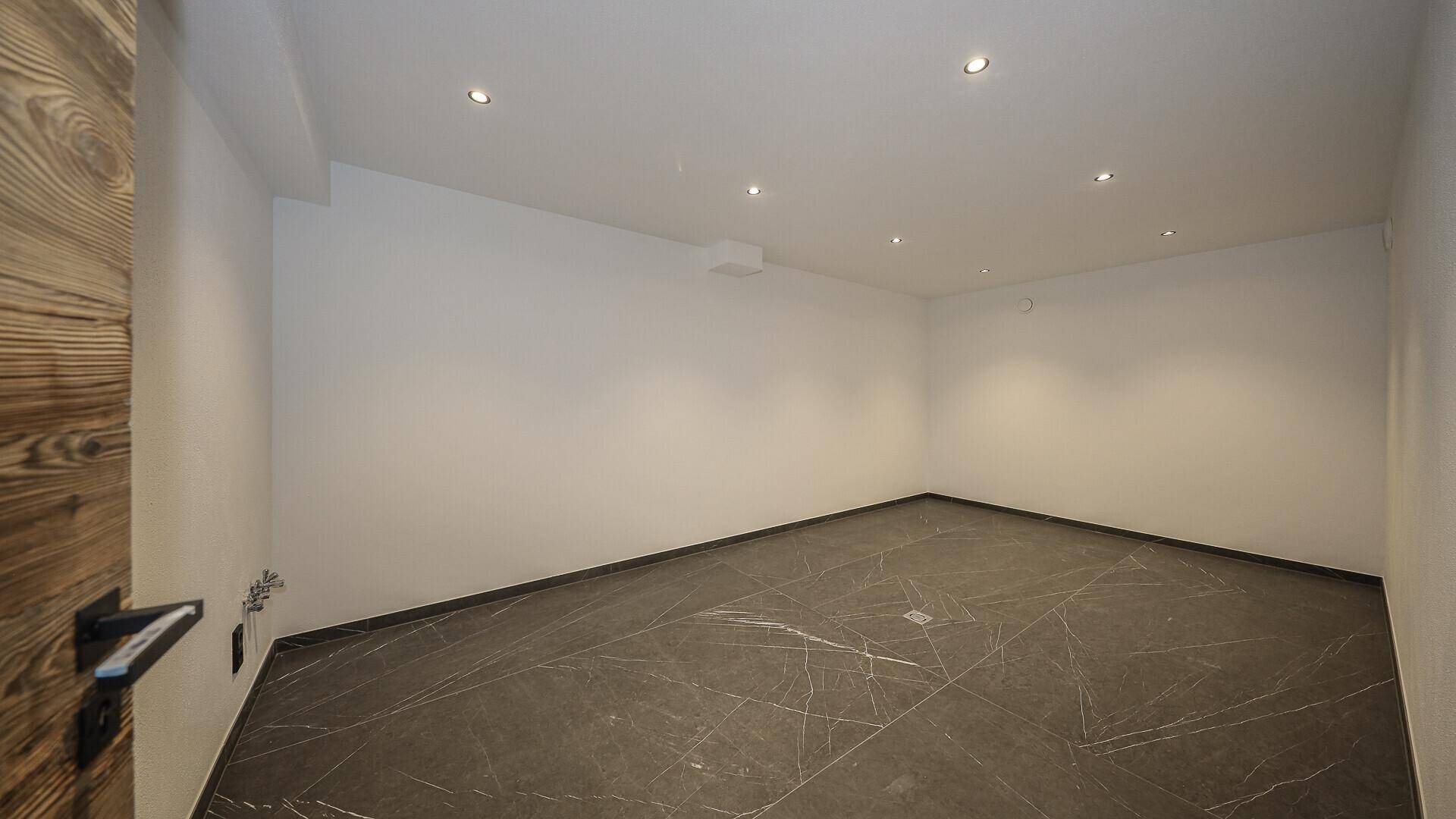 Leerer Raum mit dunklem Fliesenboden und weiß gestrichenen Wänden, vielseitig nutzbar.