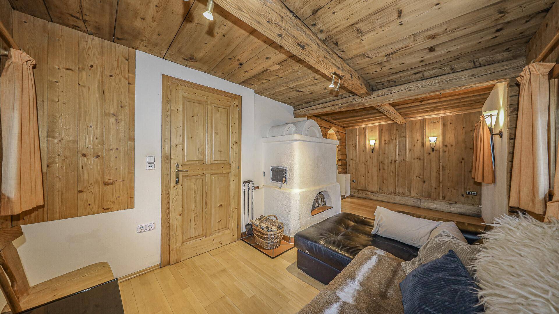 Gemütliches Wohnzimmer im alpinen Stil mit Holzwänden, Kachelofen und rustikalen Möbeln.
