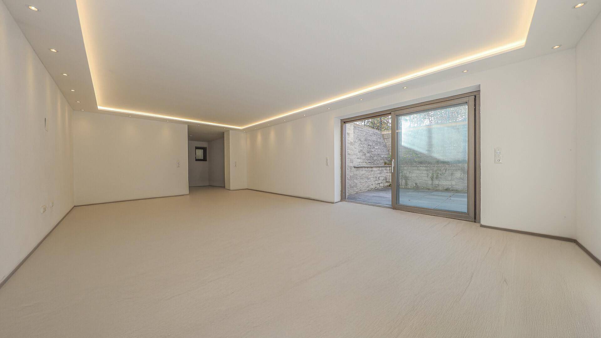 Geräumiger, heller Raum mit Fliesenboden und Zugang zu einem privaten Außenbereich.