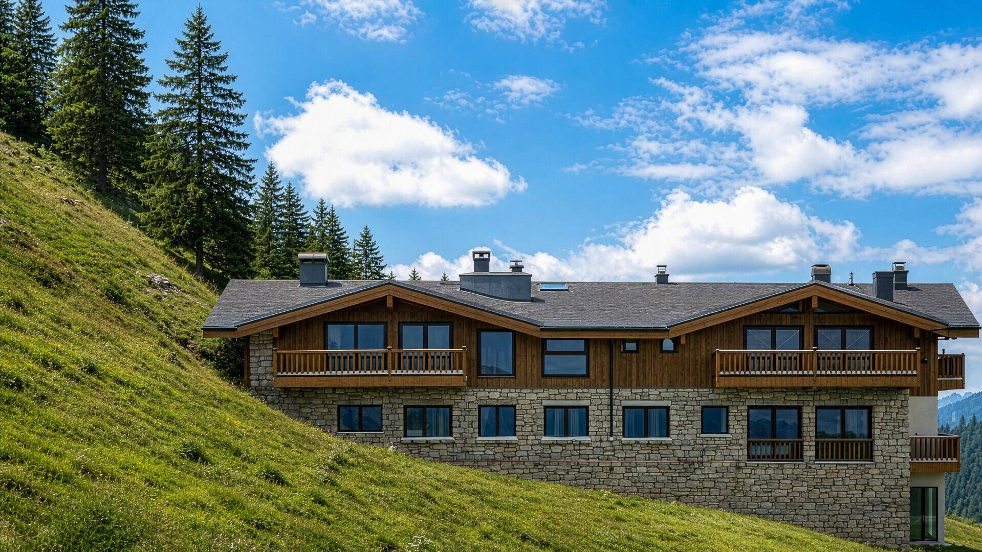Großes Chalet-Gebäude mit Stein- und Holzfassade, Balkonen und vielen Fenstern am Berghang.