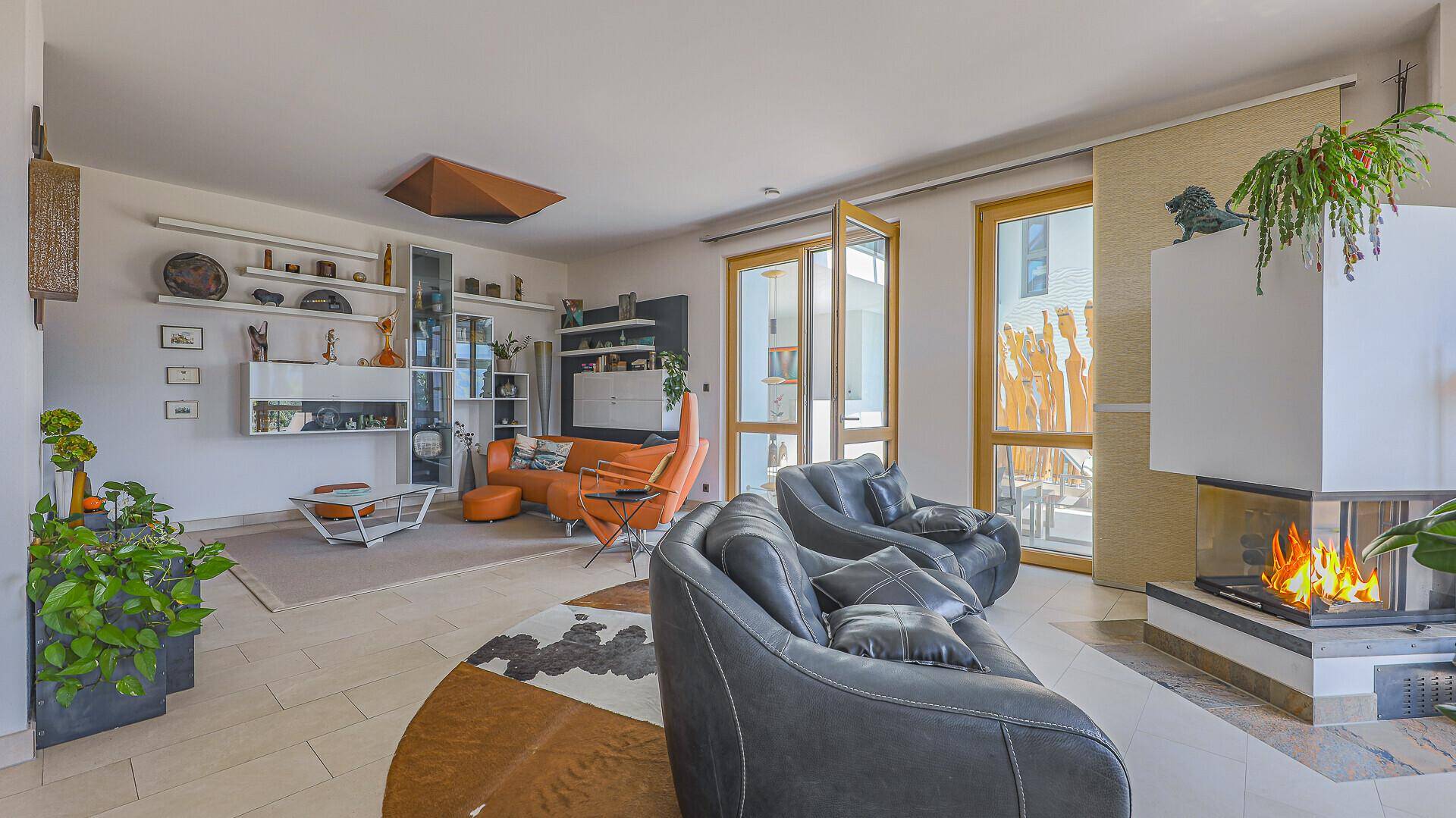 Helles Wohnzimmer mit Kamin, Fliesenboden und Zugang zu großen Fenstern mit Bergblick.