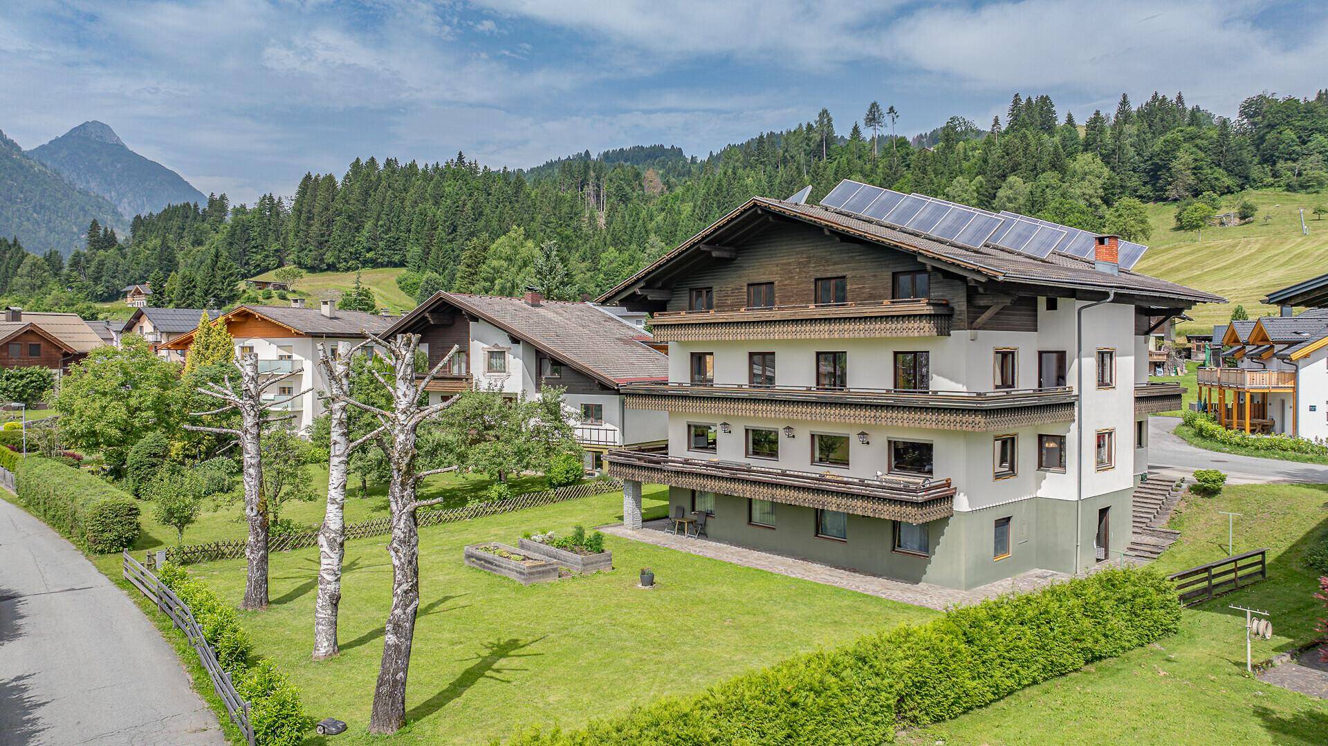 Ansicht eines traditionellen Gebäudes mit Holzbalkonen und Solarpaneelen in bergiger Landschaft.
