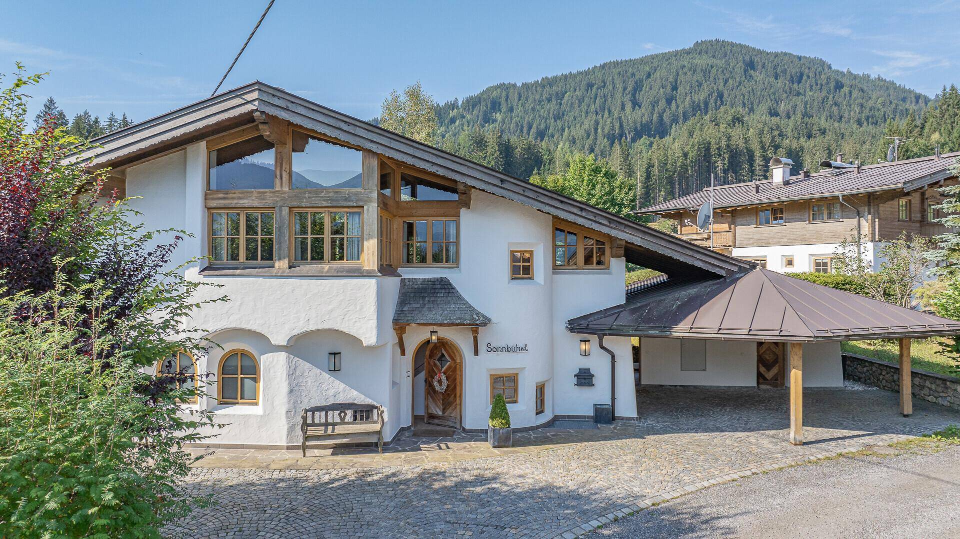 Charmantes Haus im alpinen Stil mit Carport und Bergblick unter blauem Himmel.