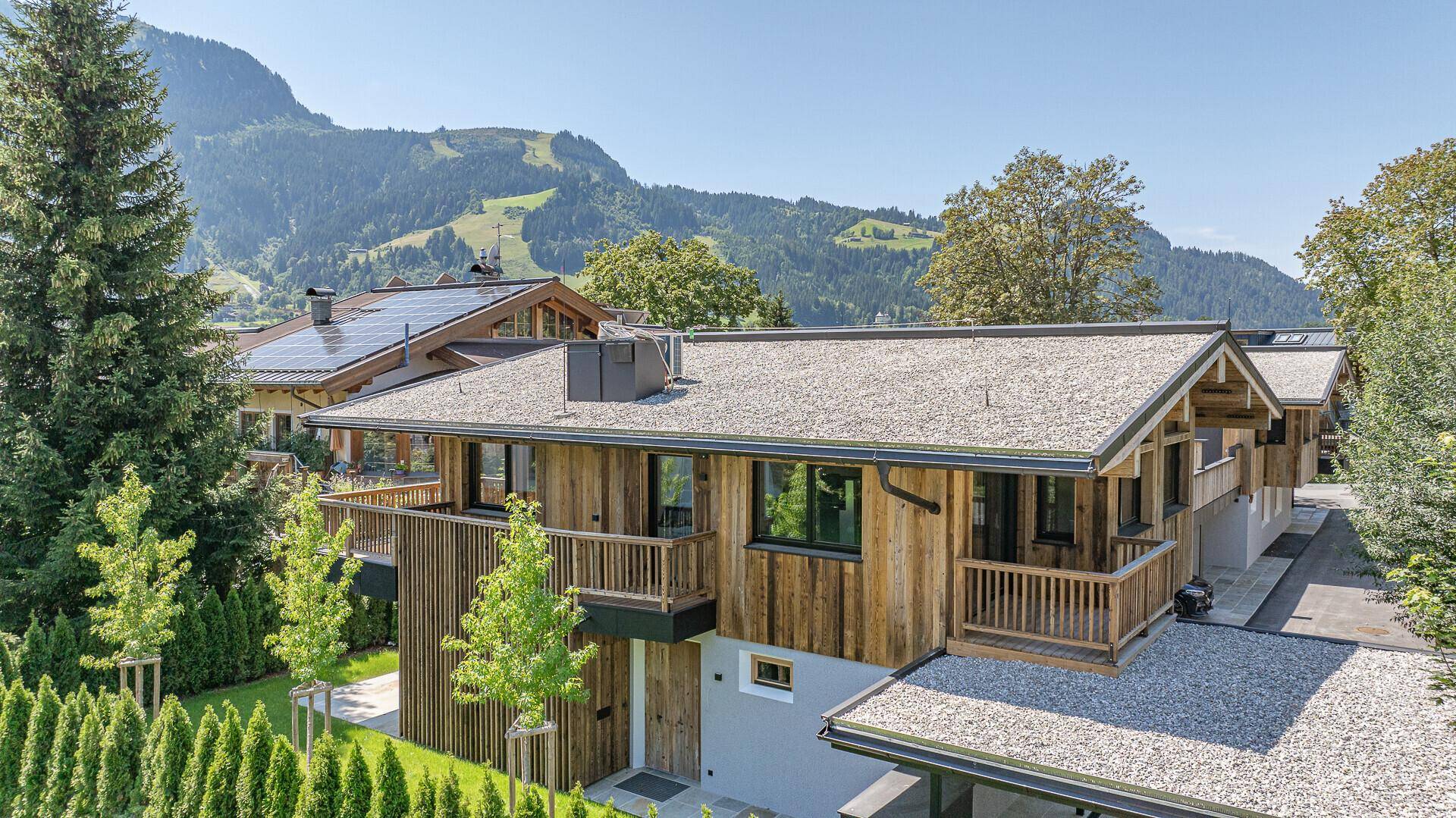 Panoramablick auf ein modernes Holzhaus mit Balkonen und umliegender Berglandschaft.