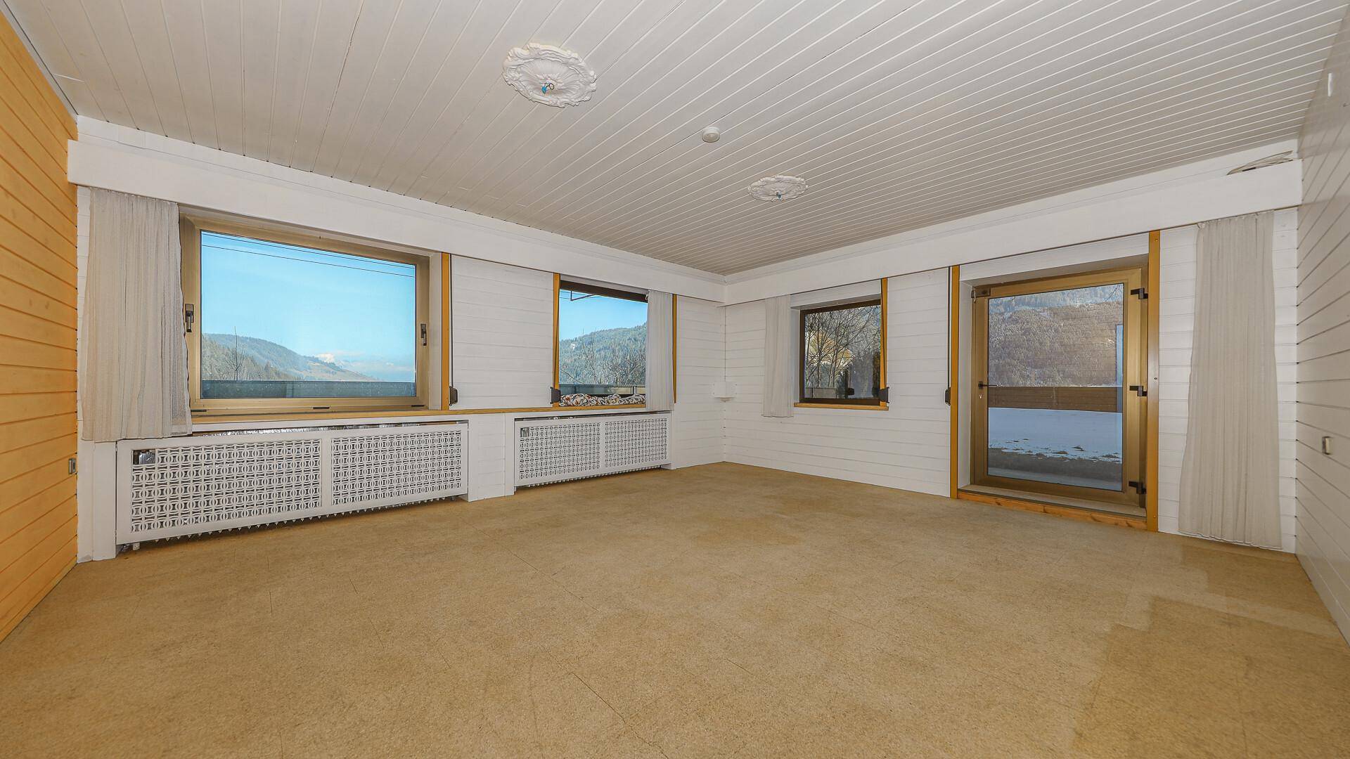 Geräumiges Wohnzimmer mit Teppichboden, Holzvertäfelung und großen Fenstern mit Bergblick.