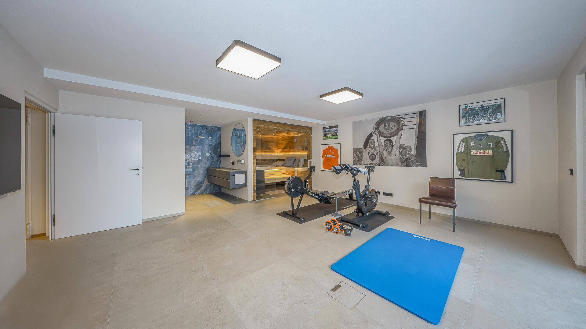 Geräumiger Fitnessraum mit Trainingsgeräten und angrenzendem Wellnessbereich inklusive Sauna.