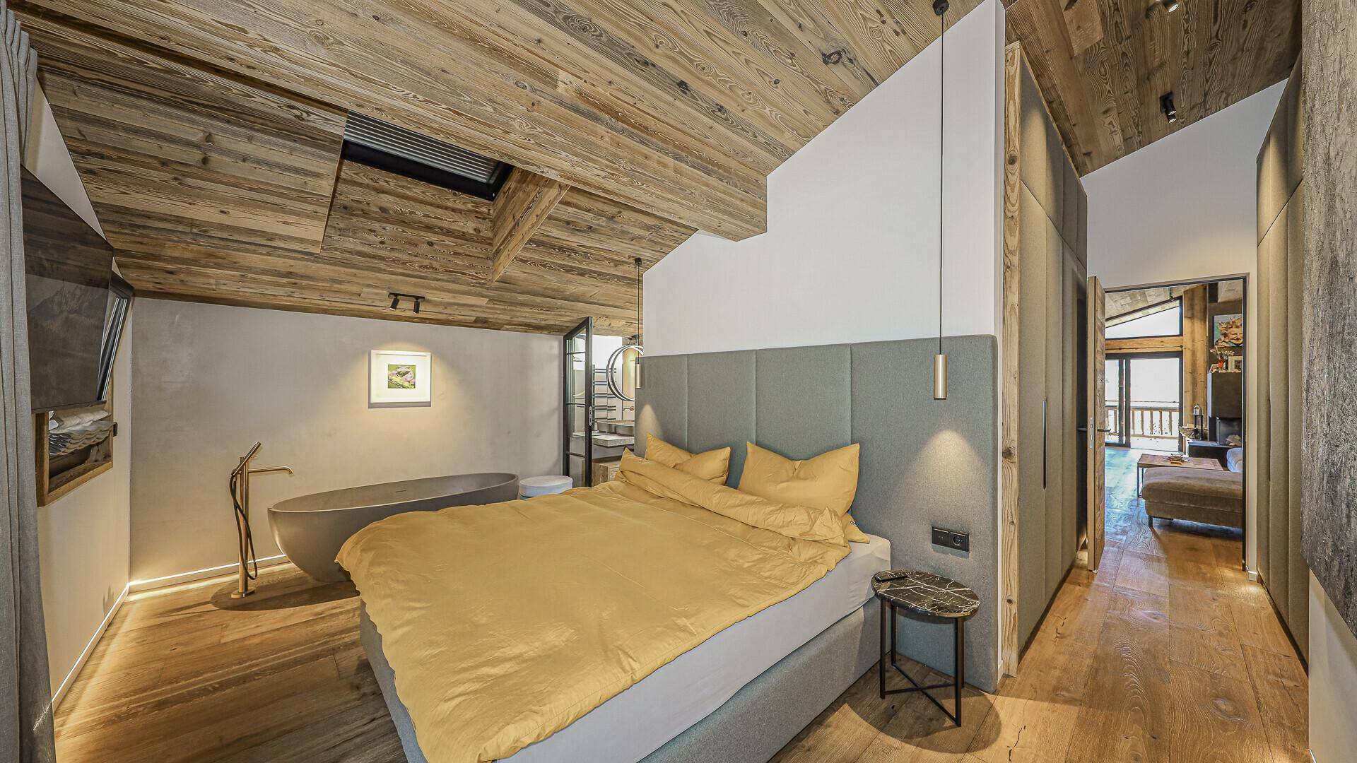 Gemütliches Schlafzimmer mit Holzbalkendecke, freistehender Badewanne und Zugang zum Bad.