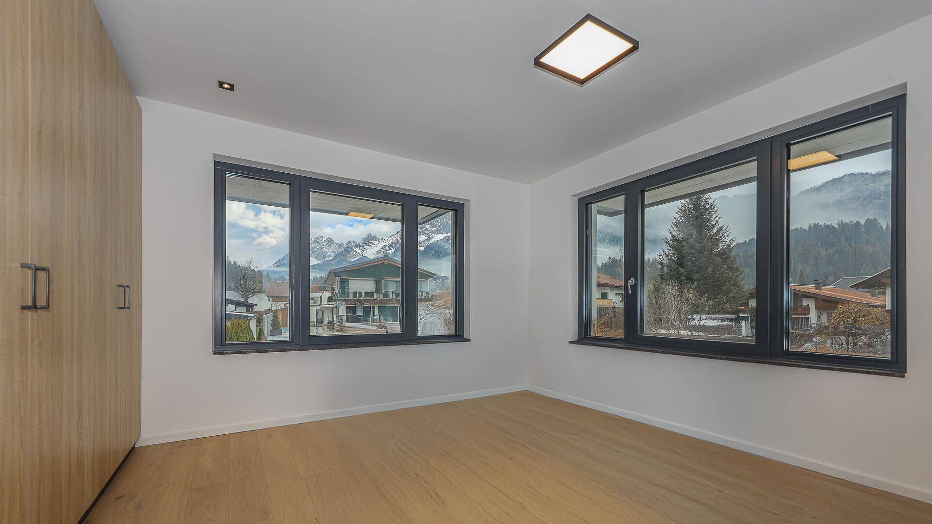 Helles Schlafzimmer mit Holzboden und großen Fenstern, die einen weiten Bergblick bieten.