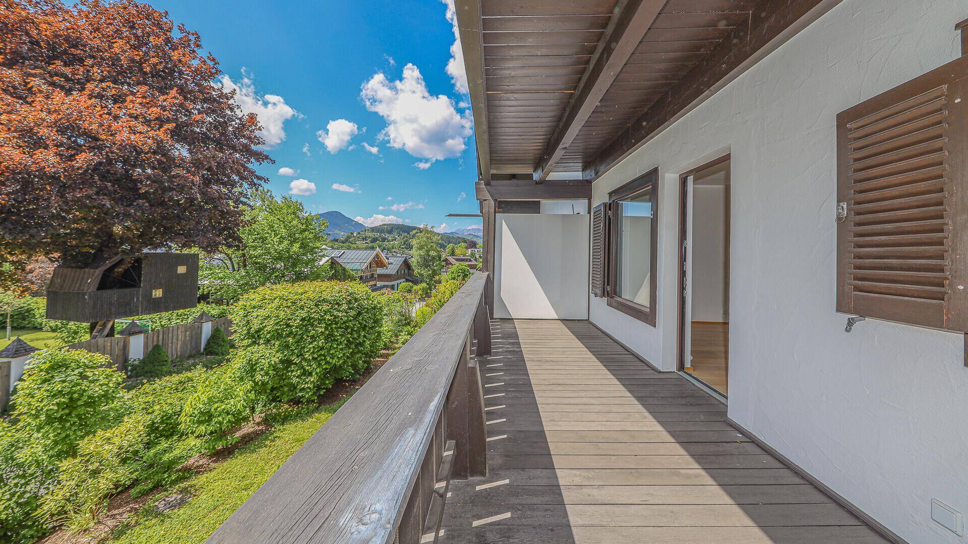 Geräumiger, unmöblierter Balkon mit Holzboden, bietet weiten Blick auf Berge und Grünflächen.