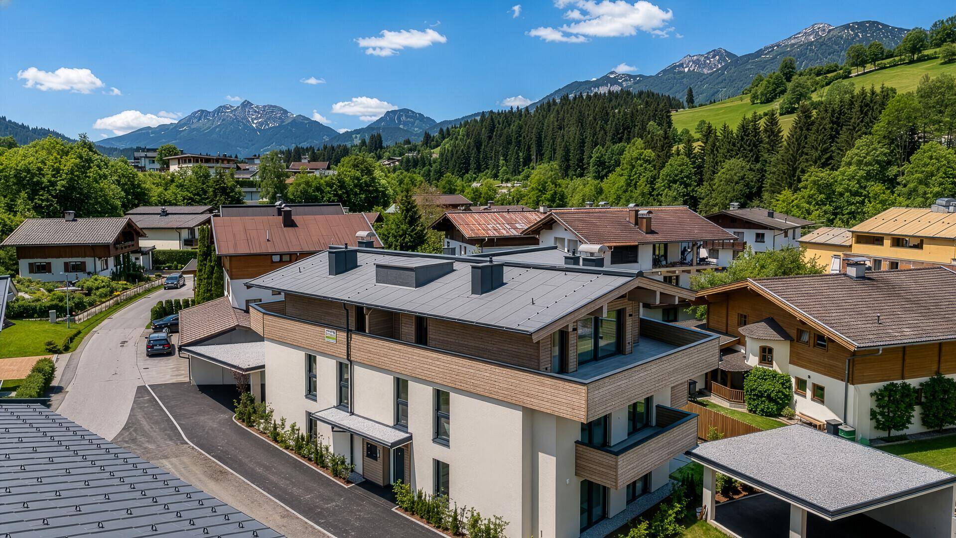 Luftaufnahme eines modernen Wohngebäudes mit Flachdach inmitten grüner Hügel und Berge.