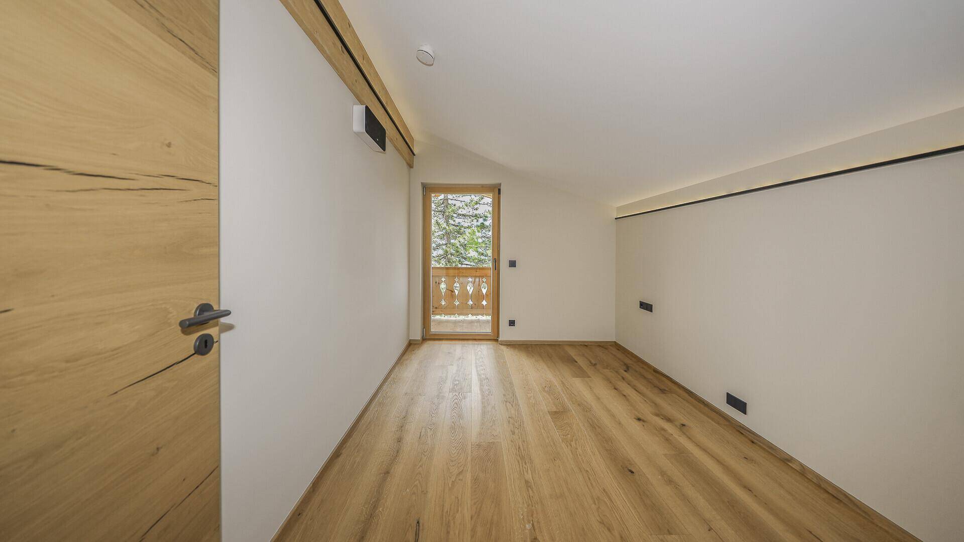 Gemütliches Zimmer im Dachgeschoss mit Holzboden und Zugang zu einem kleinen Balkon.