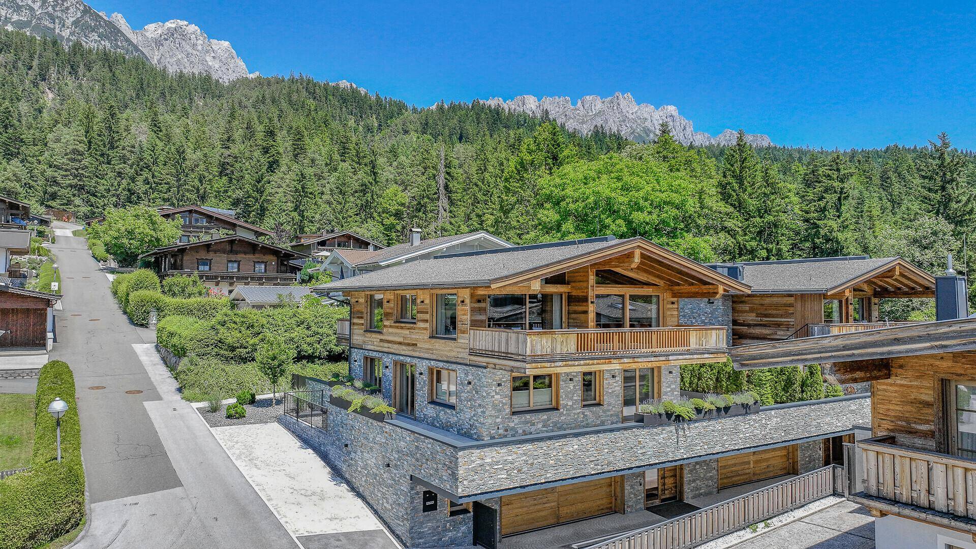 Elegantes Chalet mit Holzfassade und Steinelementen, umgeben von grüner Natur und Bergblick.