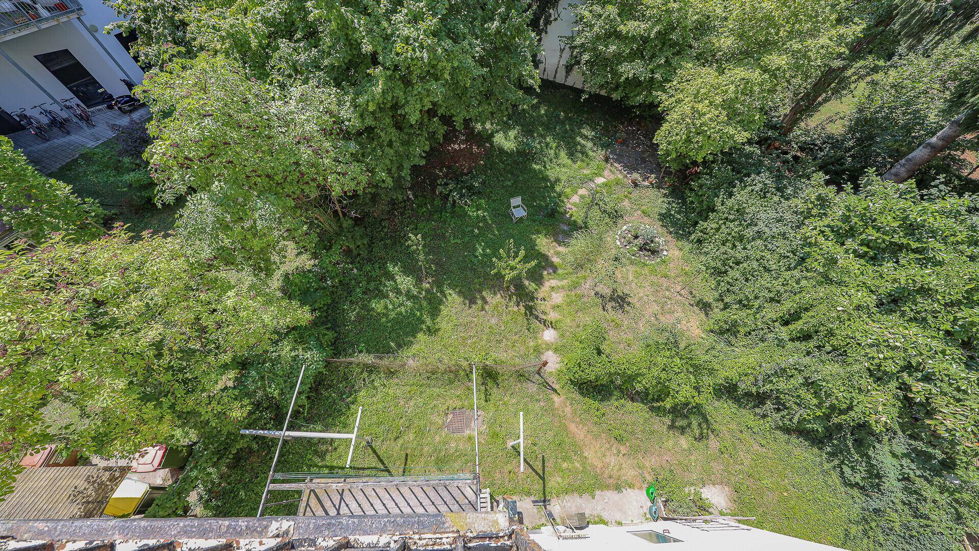 Blick von oben auf einen grünen Gartenbereich mit Bäumen und Rasenfläche.