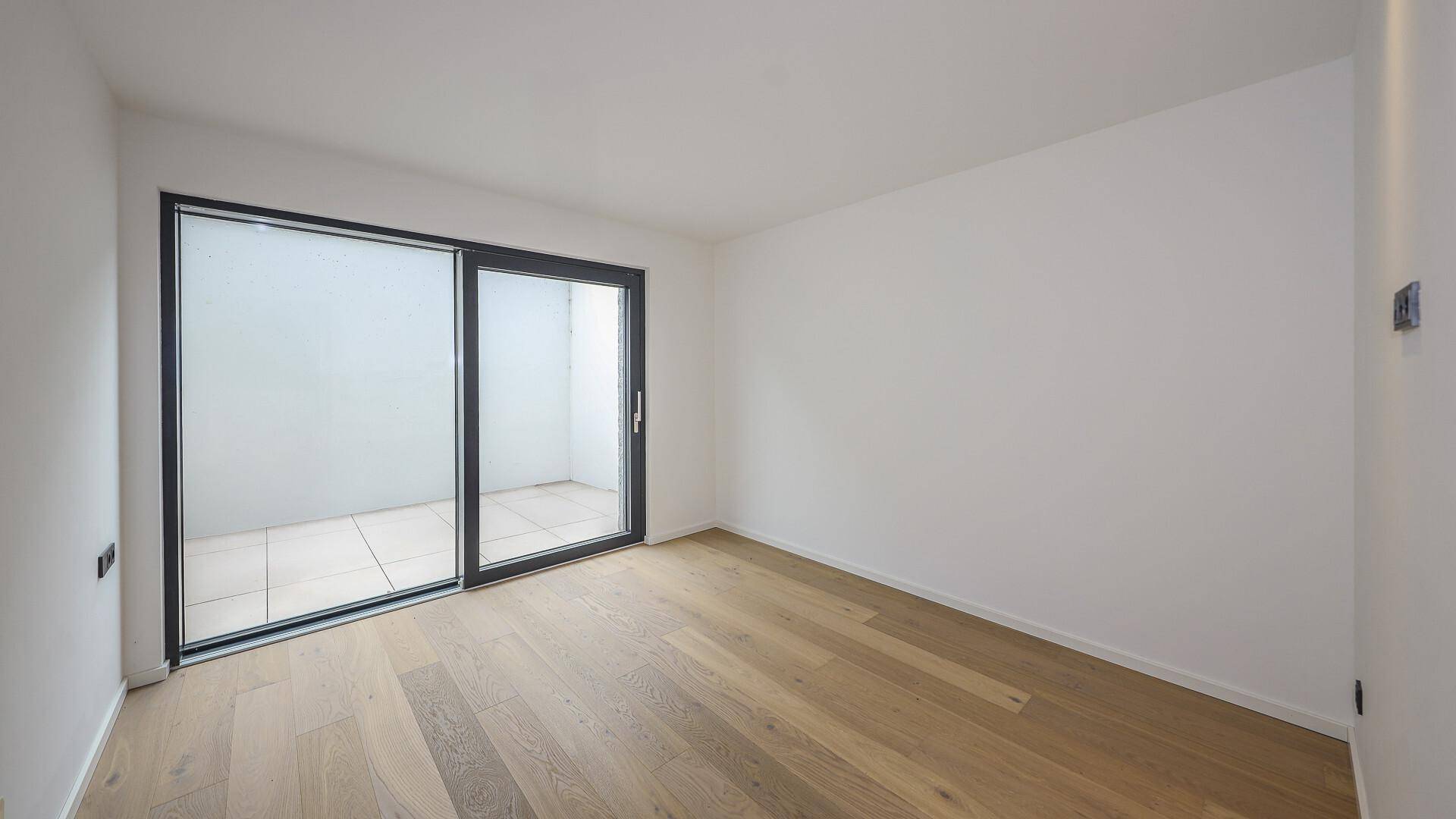 Helles Zimmer mit Holzboden und Zugang zu einem kleinen Außenbereich.