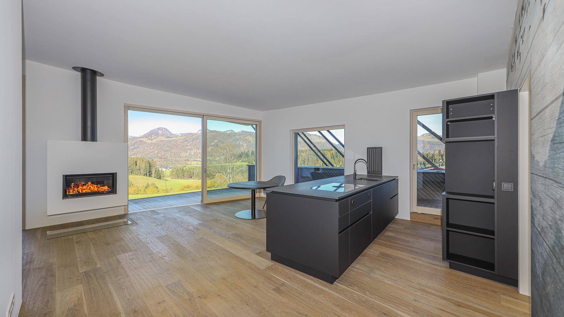 Offene Küche mit dunkler Kücheninsel, Kamin und Zugang zur Terrasse mit Bergblick.