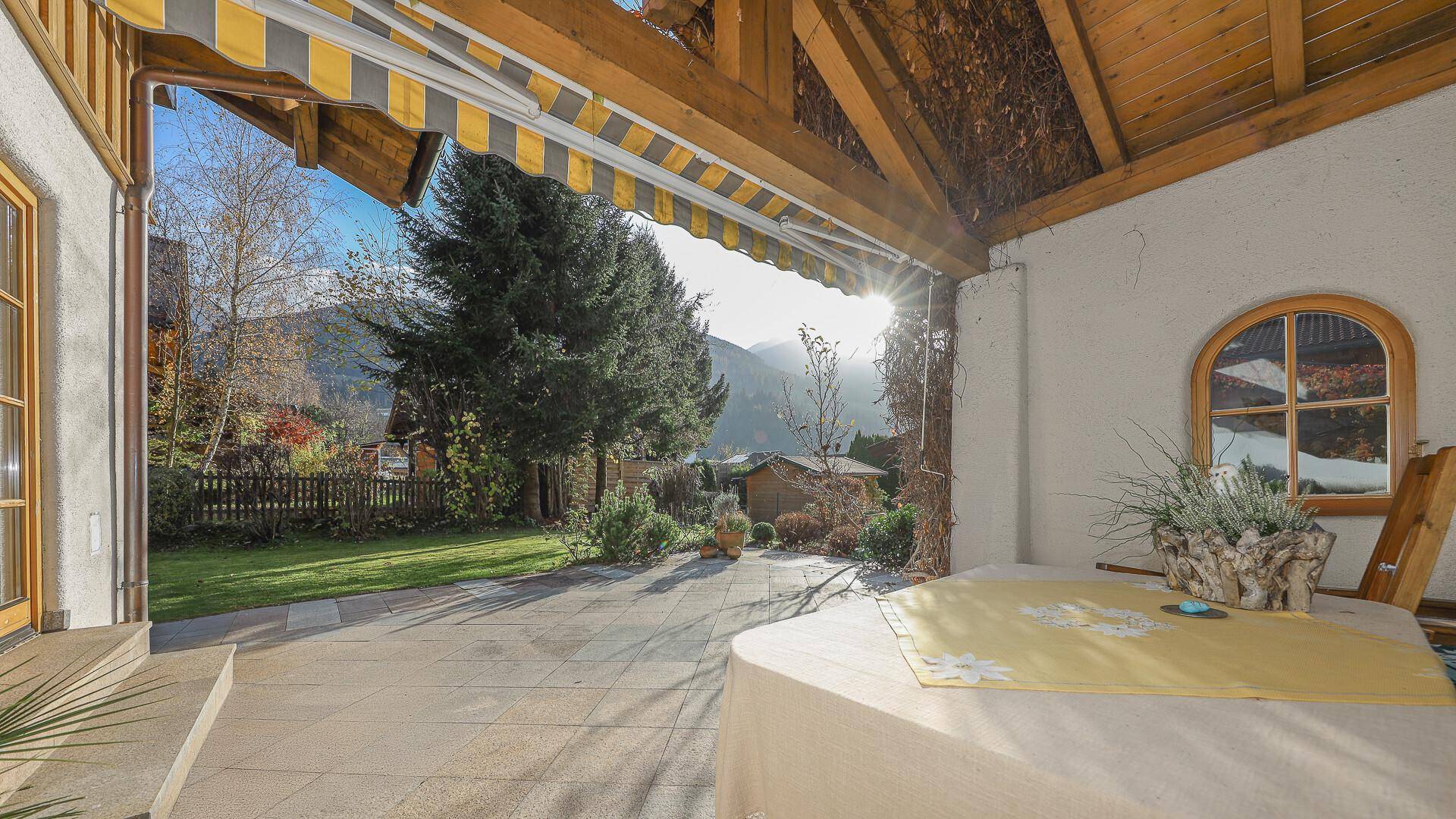 Sonniger Terrassenbereich mit Tisch, Markise und Blick auf die grüne Umgebung.