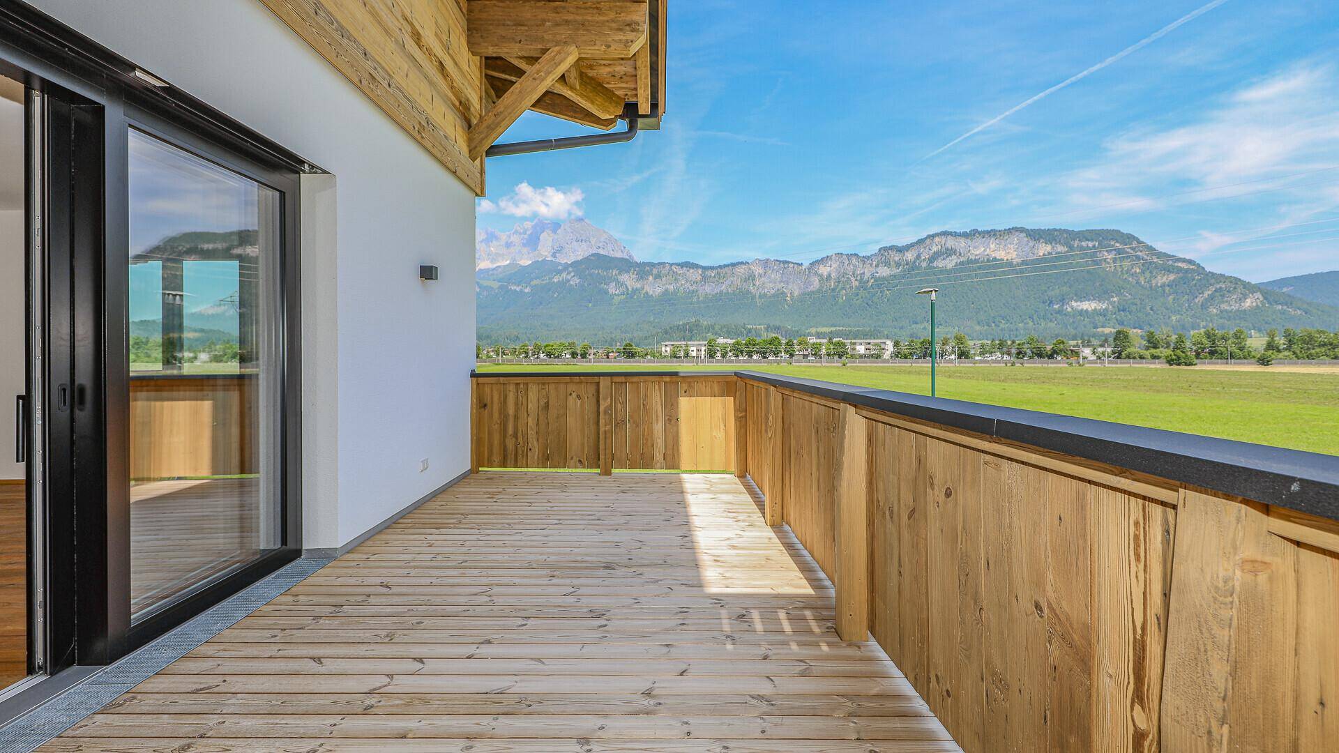 Geräumiger, unmöblierter Balkon mit Holzboden und beeindruckendem Bergblick.