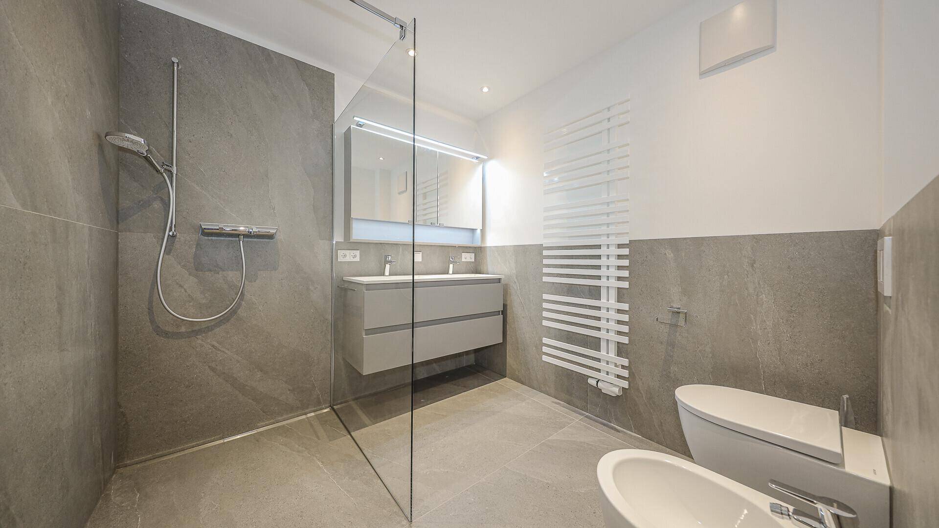Modernes Badezimmer mit grauen Fliesen, ebenerdiger Dusche und Doppelwaschbecken.