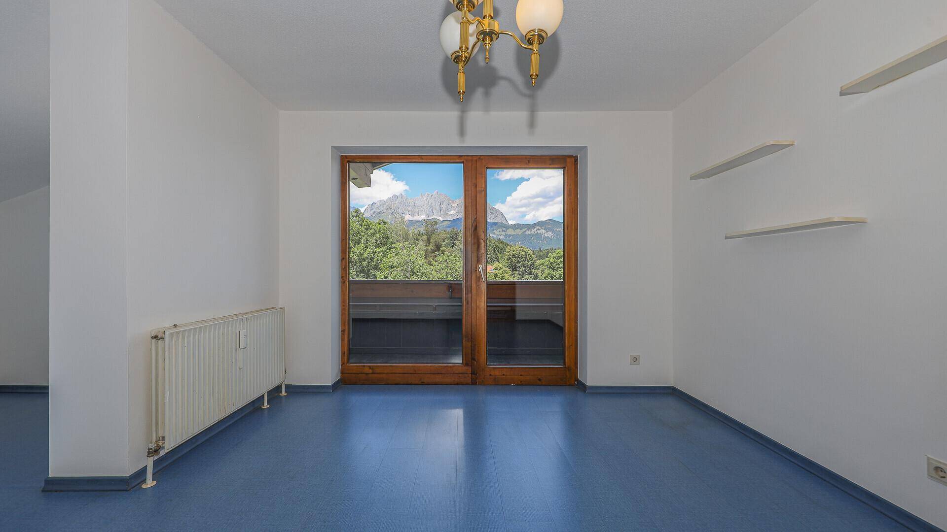 Heller Raum mit blauem Boden, Dachfenster und Blick auf die Berge durch die Balkontür.