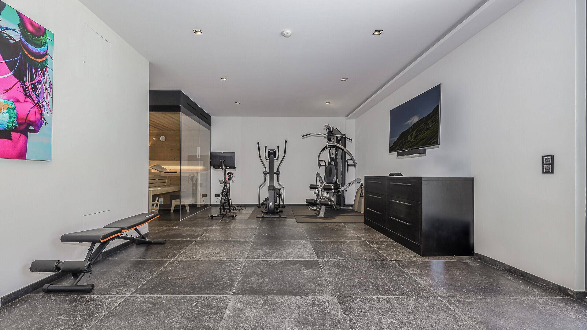 Gut ausgestatteter Fitnessraum mit verschiedenen Geräten und einer integrierten Sauna.
