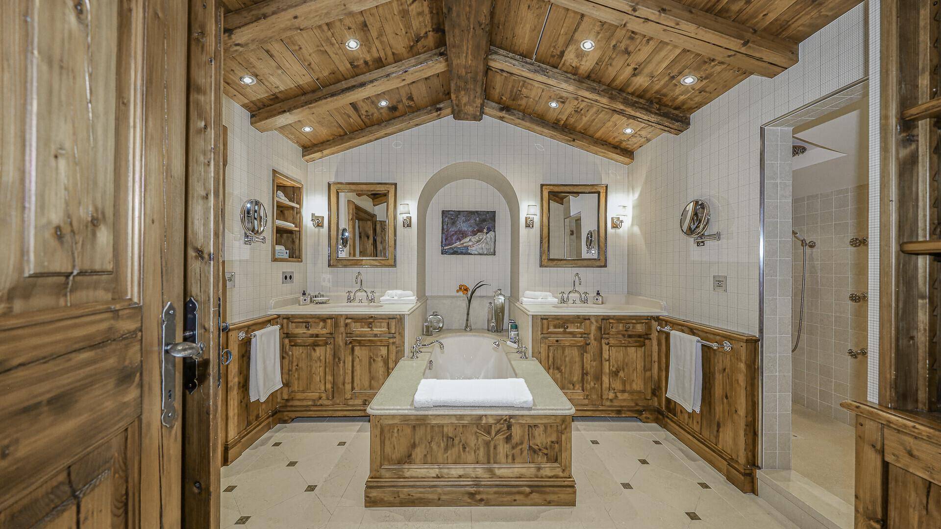 Luxuriöses Badezimmer mit Holzelementen, Doppelwaschbecken und integrierter Badewanne unter Holzbalkendecke.