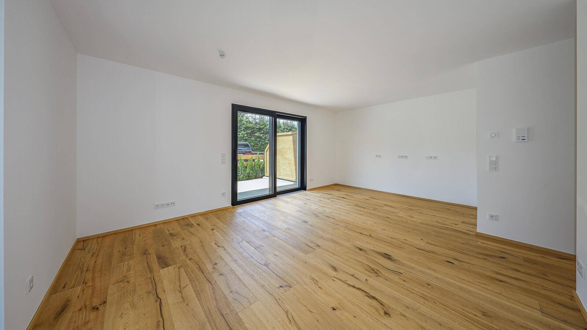 Geräumiger, unmöblierter Raum mit Holzboden und Zugang zu einem Außenbereich.