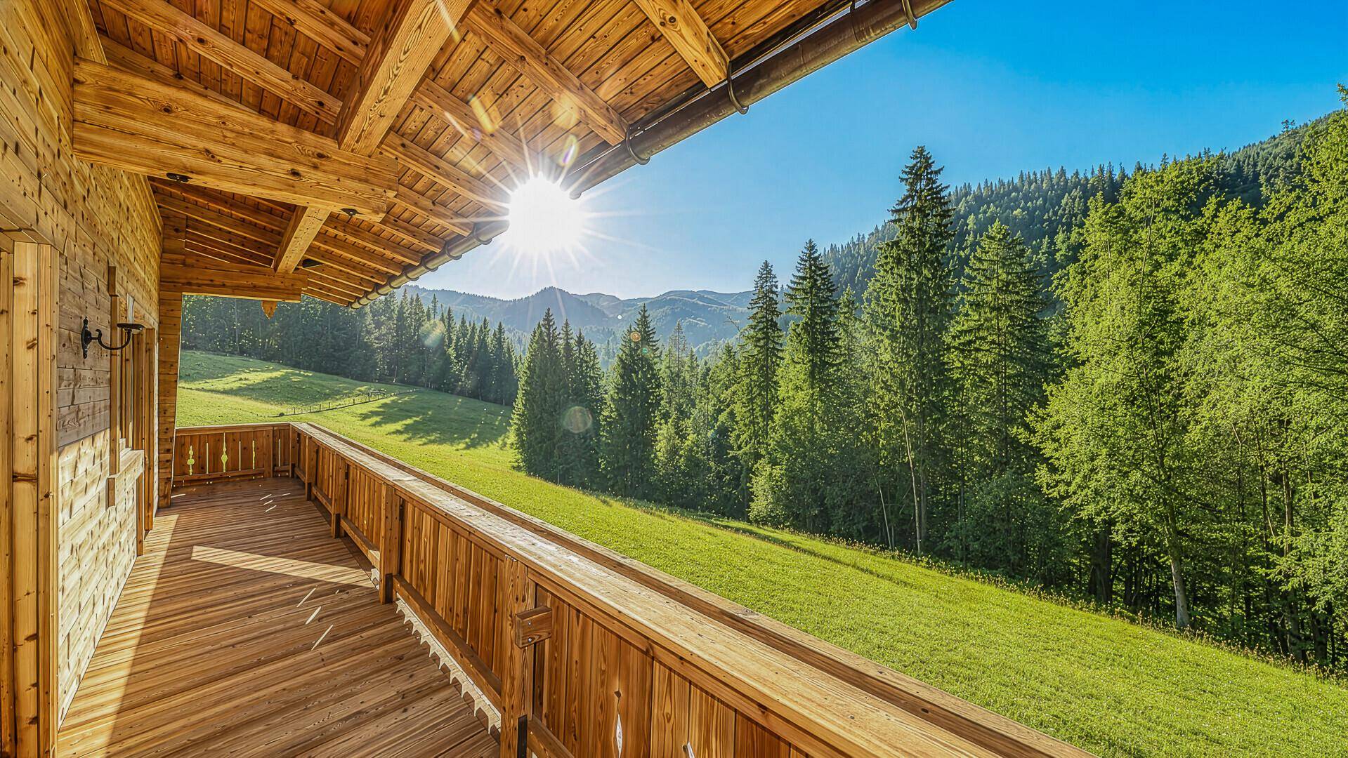 Breiter Holzbalkon mit sonnigem Bergblick und weitem Blick über die grüne Landschaft.
