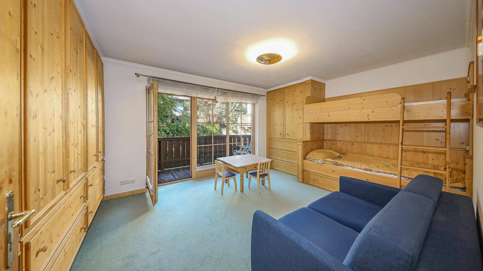 Helles Kinderzimmer mit Etagenbett, Teppichboden und Zugang zum Balkon.