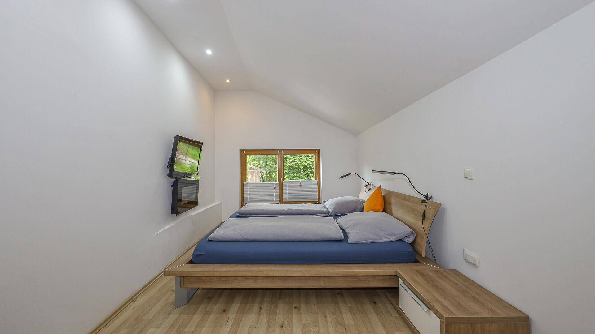 Helles Schlafzimmer mit Holzboden, Dachschräge und Blick auf die umliegende Natur.