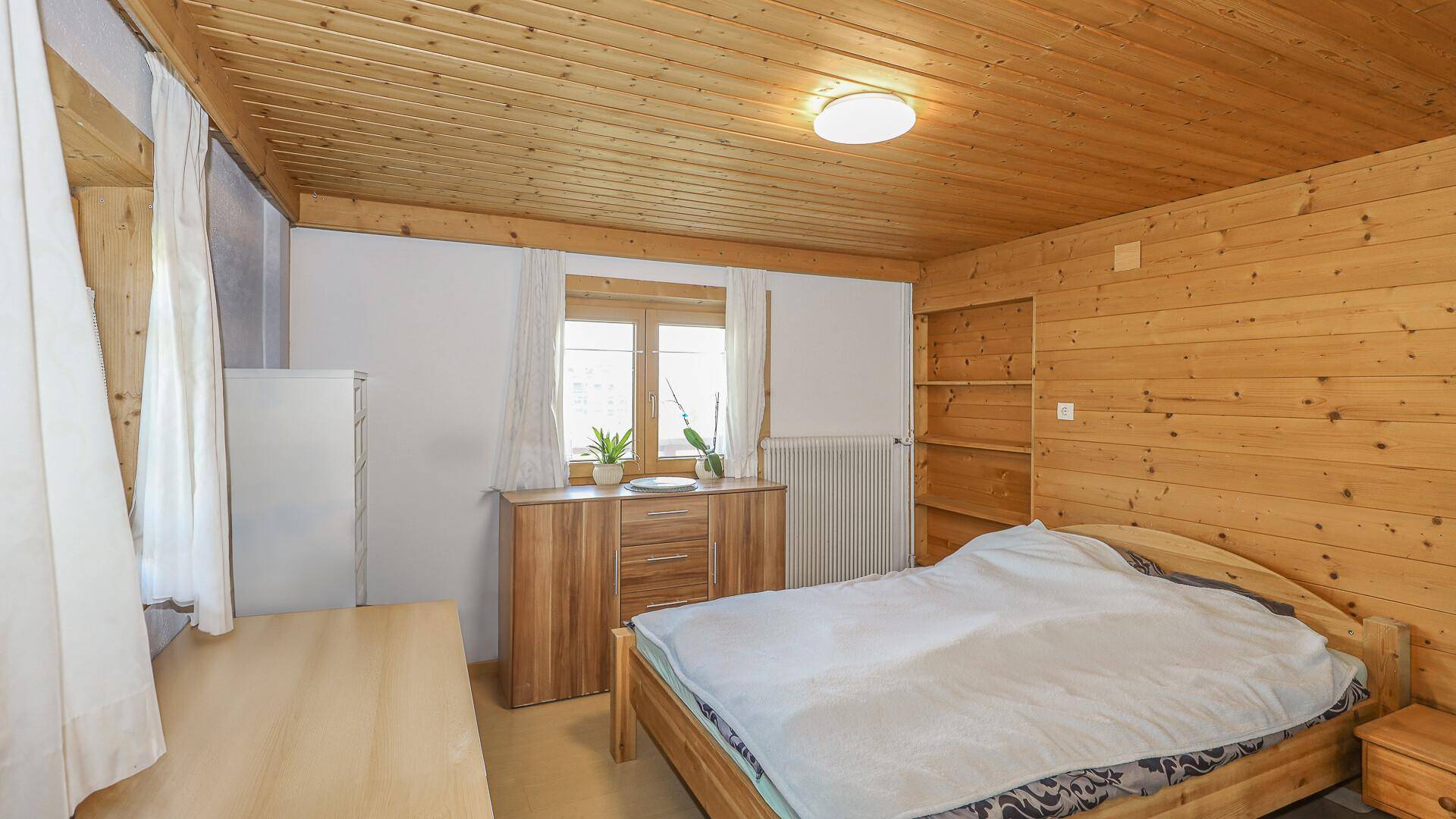 Geräumiges Schlafzimmer mit Holzwänden, Doppelbett und Fenster mit Blick ins Grüne.