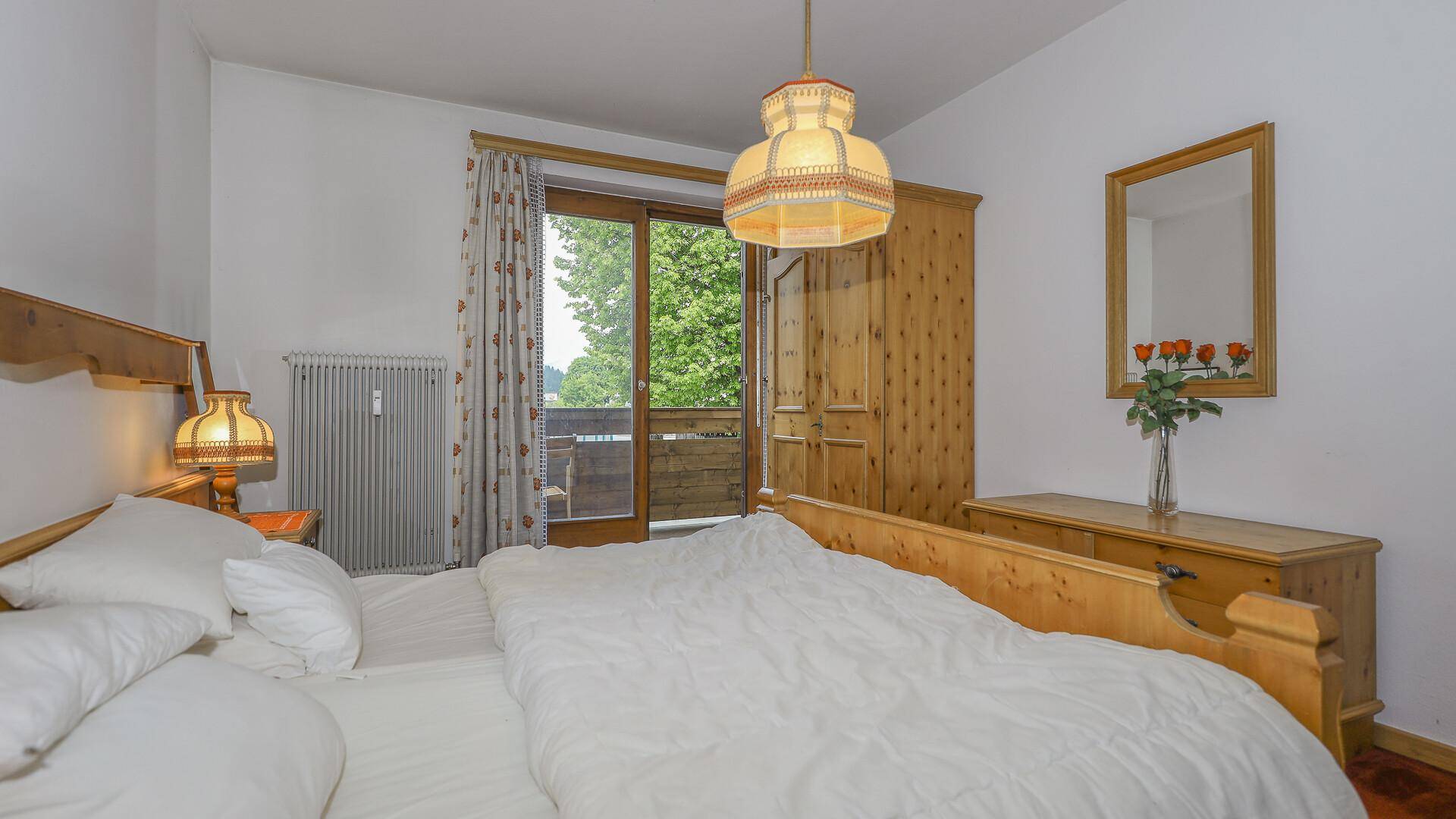 Helles Schlafzimmer mit Holzbett, Kleiderschrank und Zugang zum Balkon mit Bergblick.