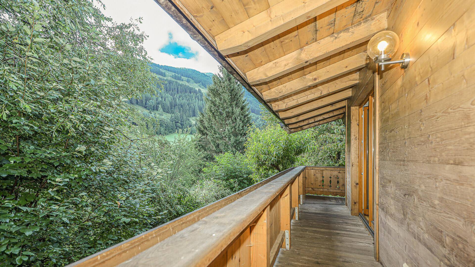 Überdachter Holzbalkon mit weitem Blick auf die umliegenden Wälder und Berge.