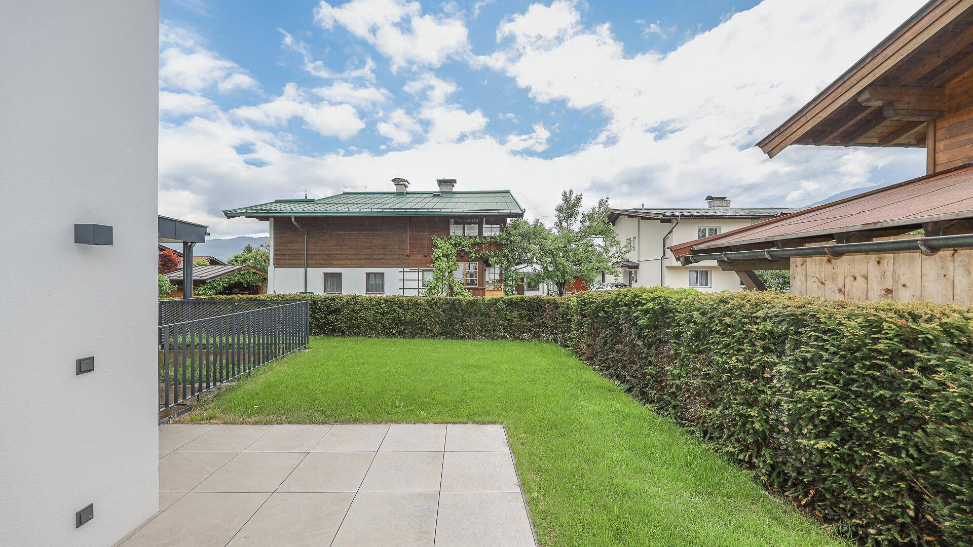 Kleiner Gartenbereich mit Rasen und Terrasse, umgeben von einer Hecke.