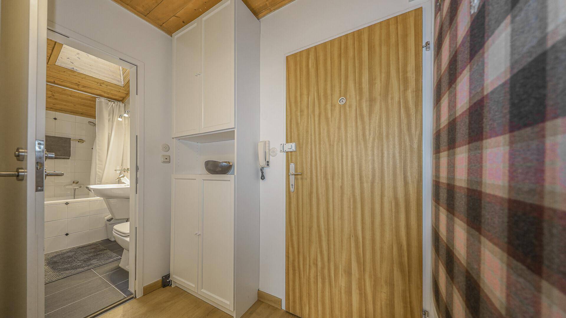 Eingangsbereich mit Holztür, Einbauschränken und Blick in das angrenzende Badezimmer.