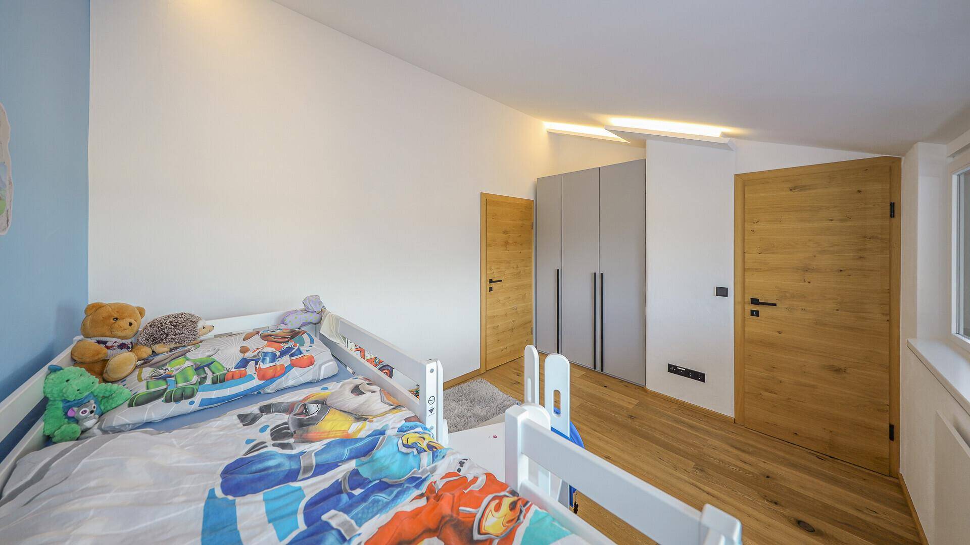 Helles Kinderzimmer mit Holzboden, Hochbett und integrierten Schränken.