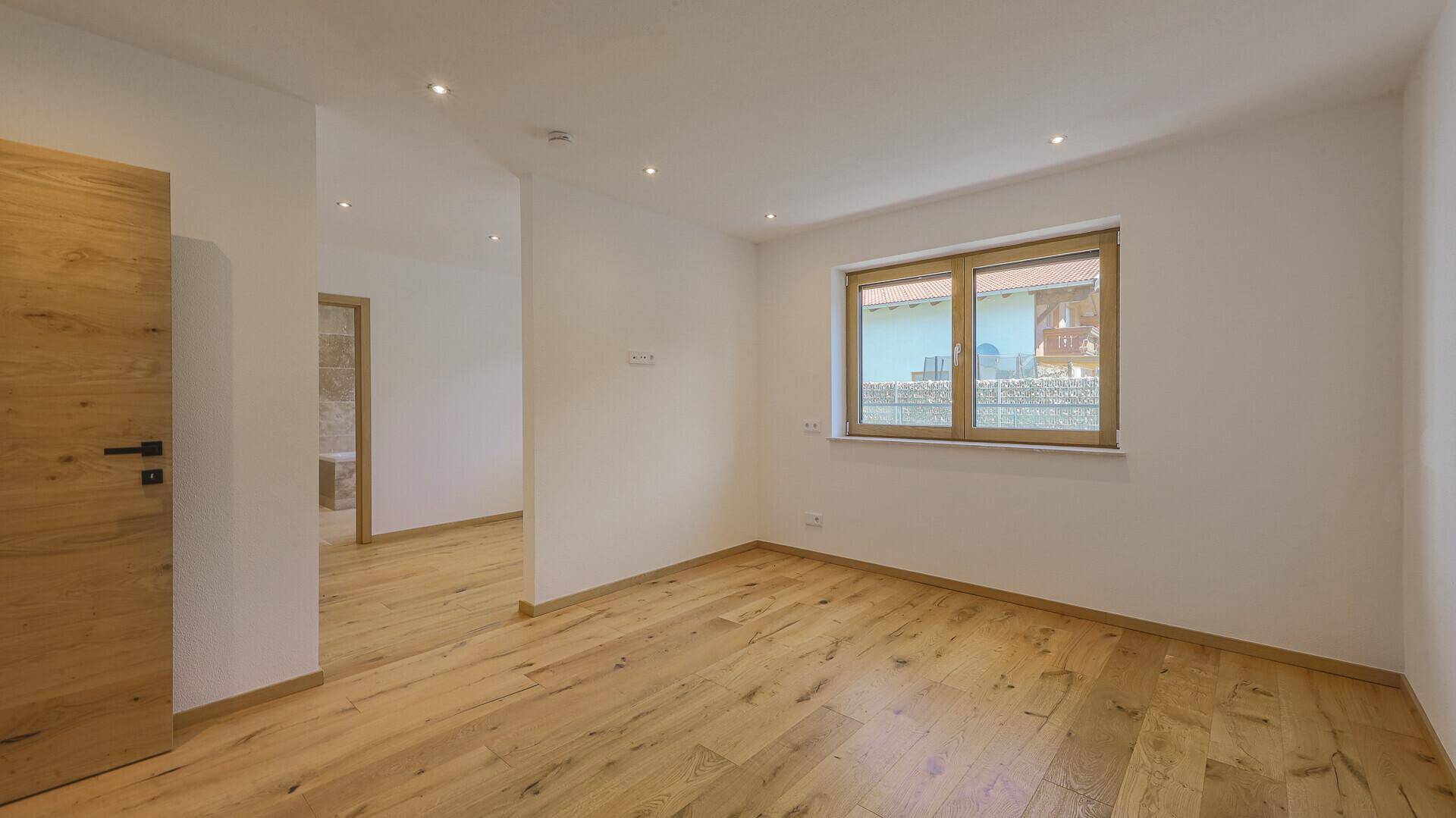 Helles Schlafzimmer mit Holzboden und Fenster, das einen Blick nach draußen bietet, bereit zur Einrichtung.