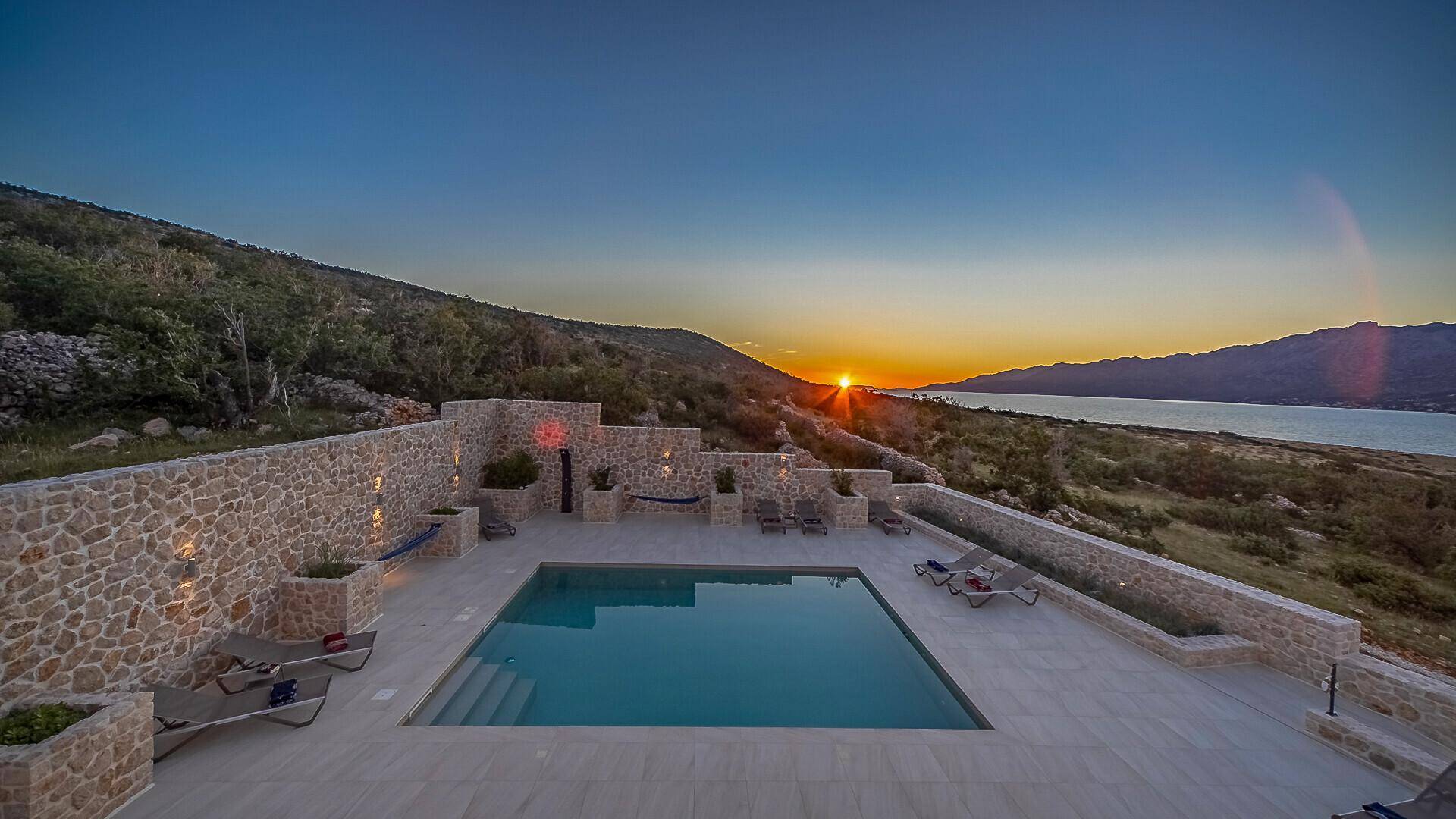 Malerischer Poolbereich bei Sonnenuntergang, umgeben von Steinmauern und mit Blick auf die Landschaft.