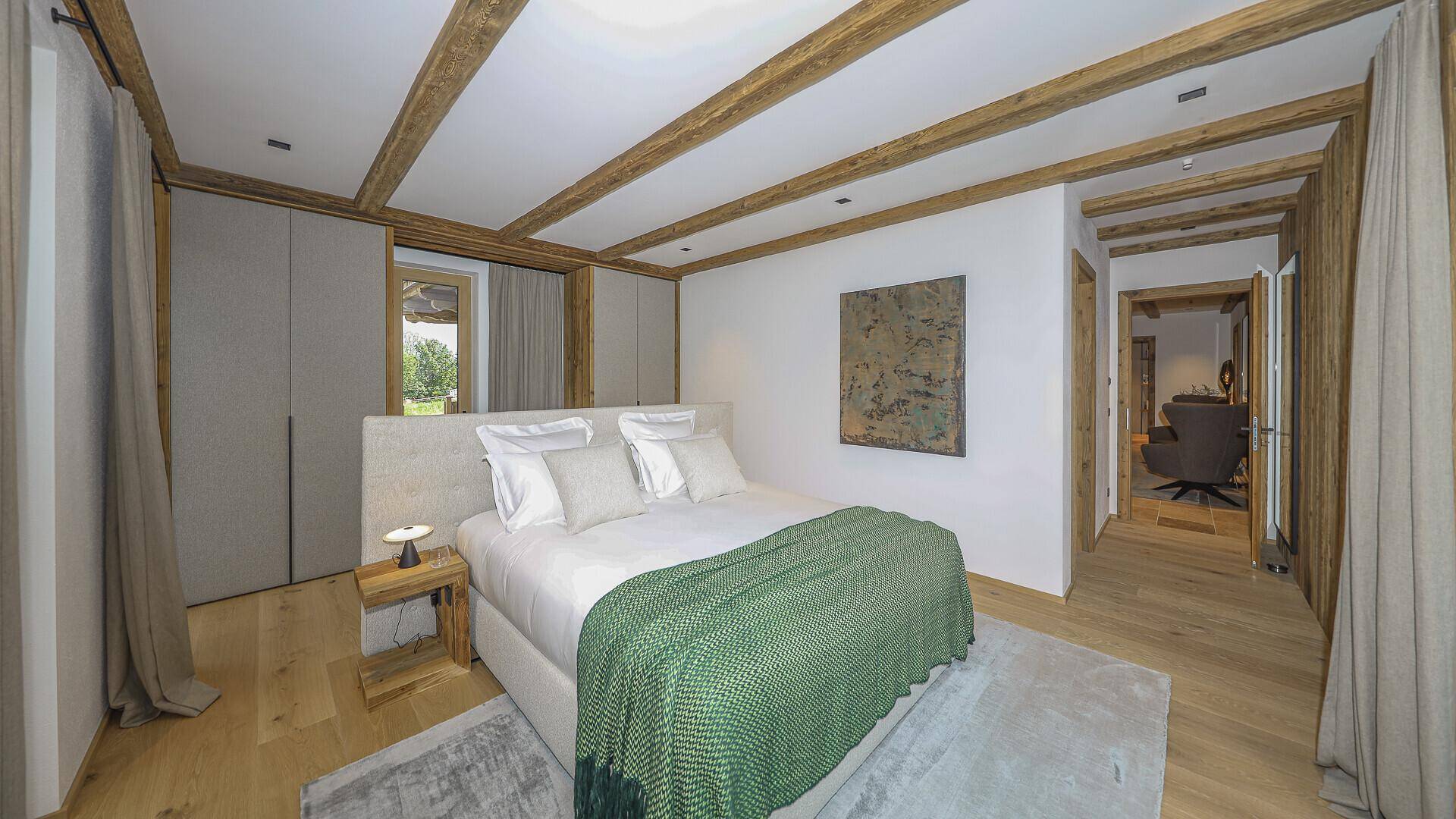 Helles Schlafzimmer mit Holzbalken, integrierten Schränken und Blick auf die grüne Umgebung.